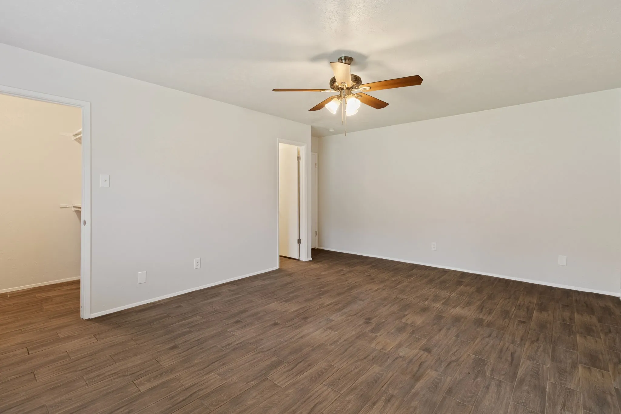 Spacious room featuring wood-finish flooring, light-toned walls, and a ceiling fan with integrated lighting