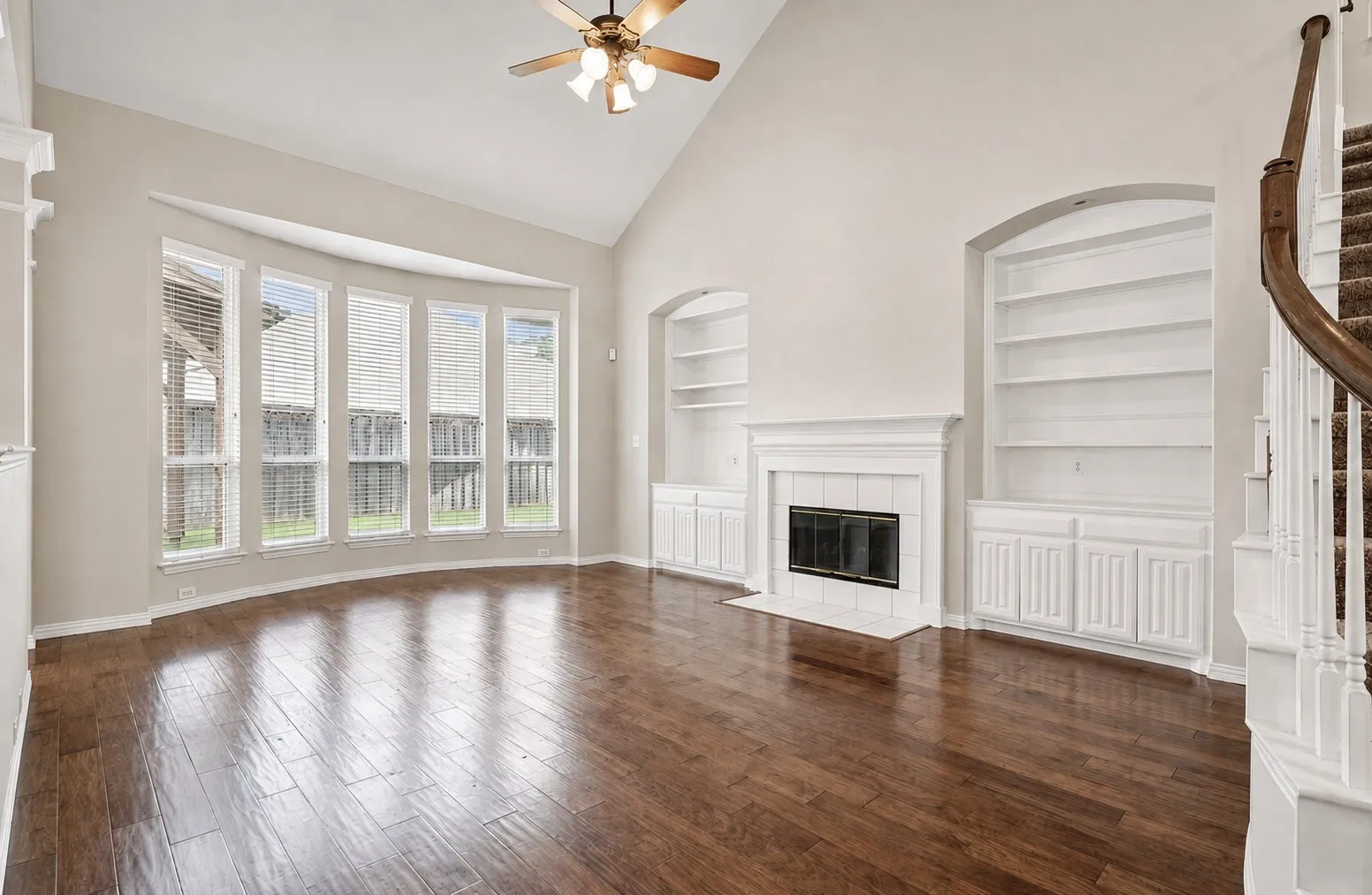 Vaulted ceiling, bay window, wood-finish flooring, fireplace with white tile surround, and built-in shelving