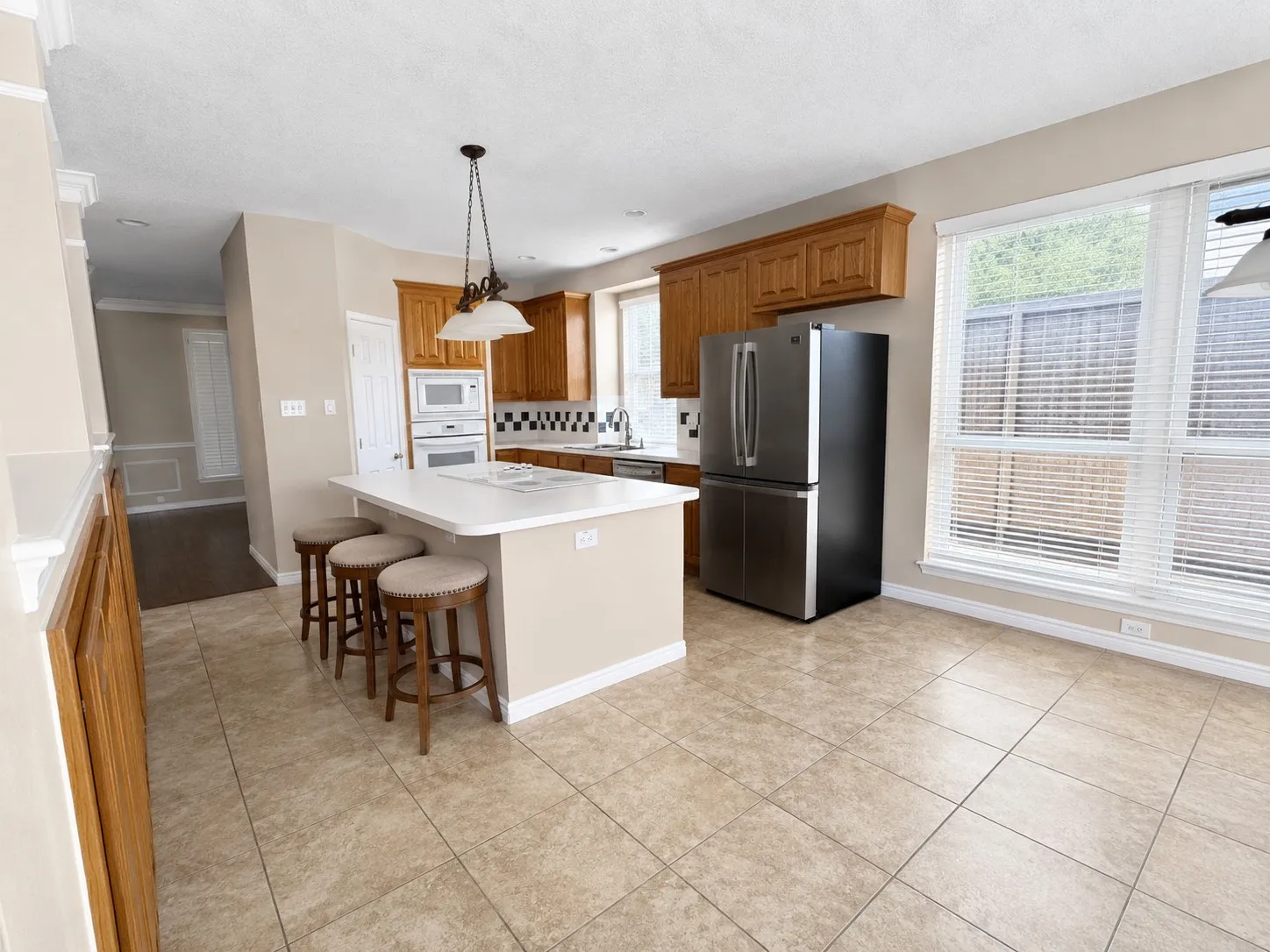 Kitchen featuring a central island with white countertop, warm-toned wood cabinetry, built-in double ovens, and tile flooring