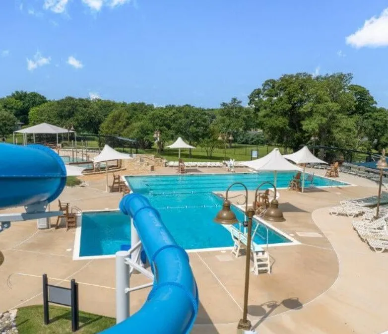 Swimming pool area featuring multiple pools, a water slide, umbrellas, and ample deck space