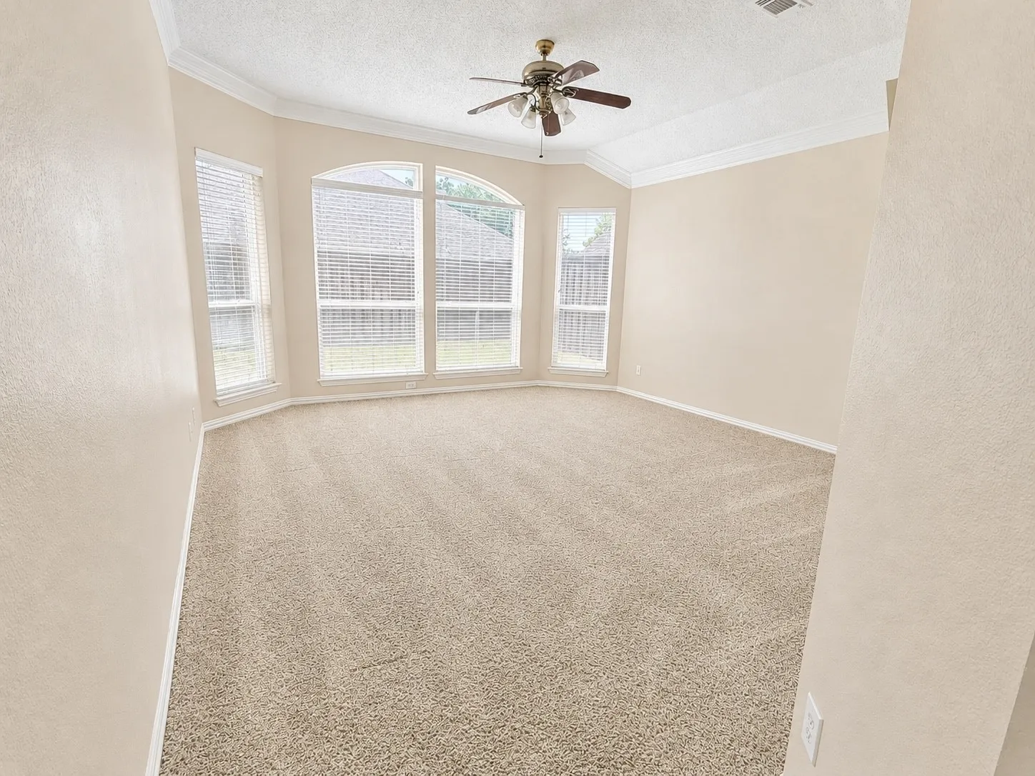 Recessed bay window with arched accent, crown molding, ceiling fan, and neutral carpet flooring