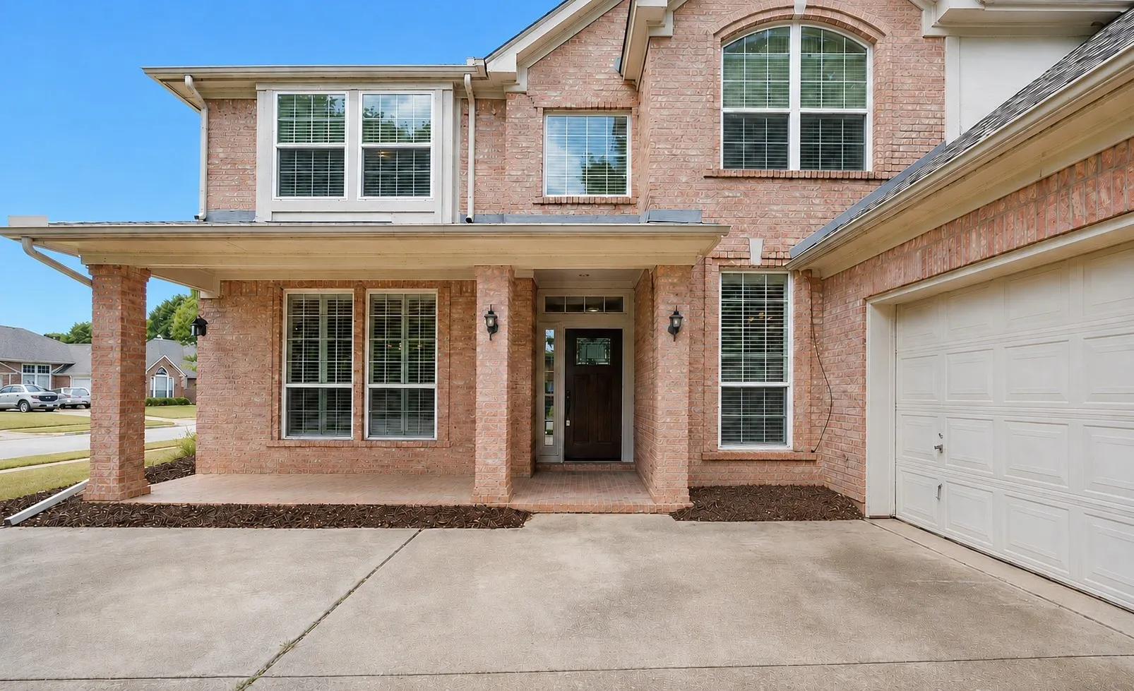 Brick exterior featuring a covered front porch with columns, a prominent arched window, and an attached two-car garage