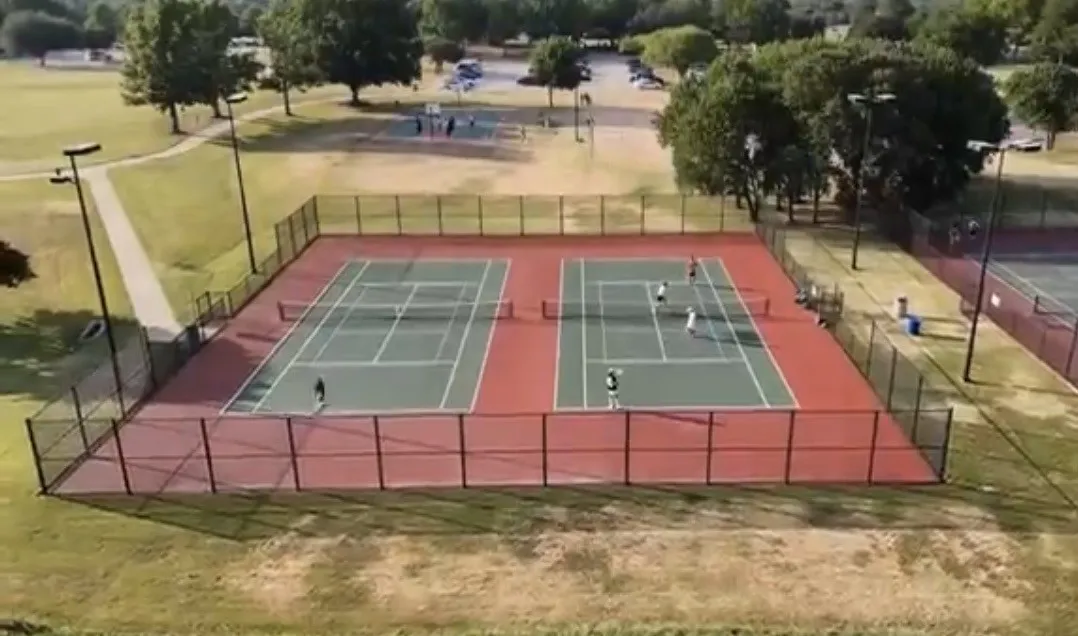 Two tennis courts with a red and green surface, surrounded by chain-link fencing