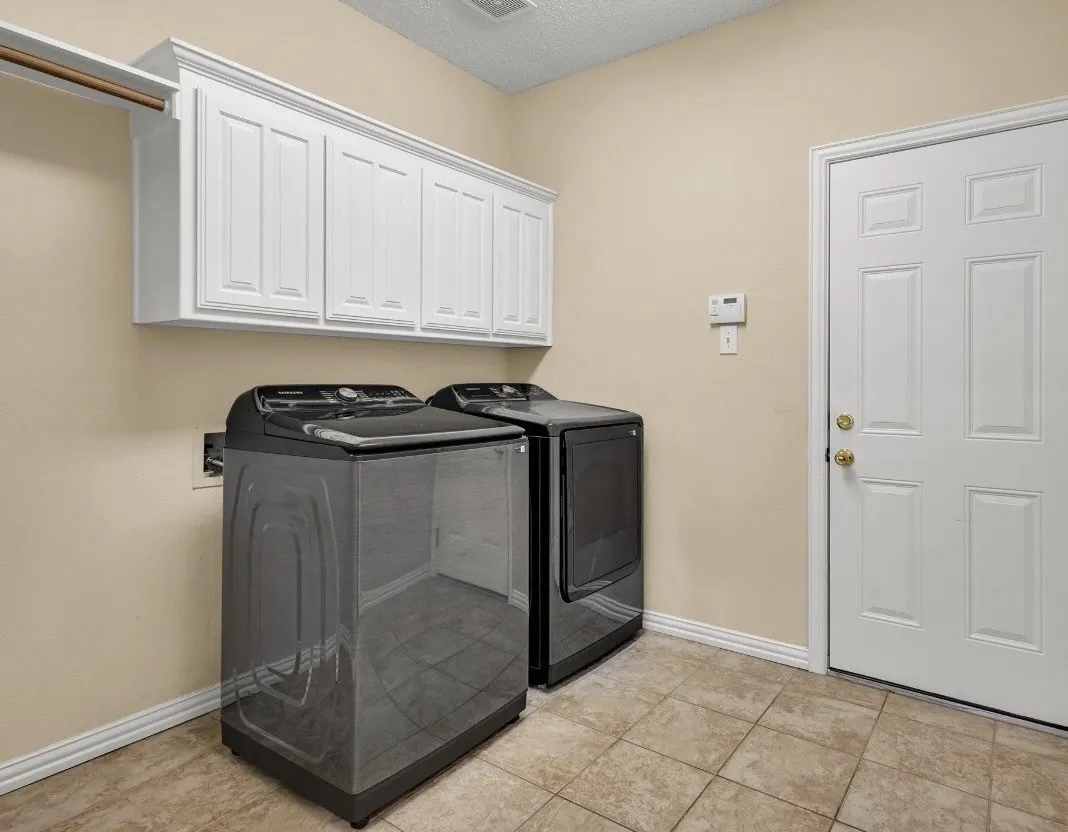Tile flooring with light-toned walls, white upper cabinetry, and a clothing rod