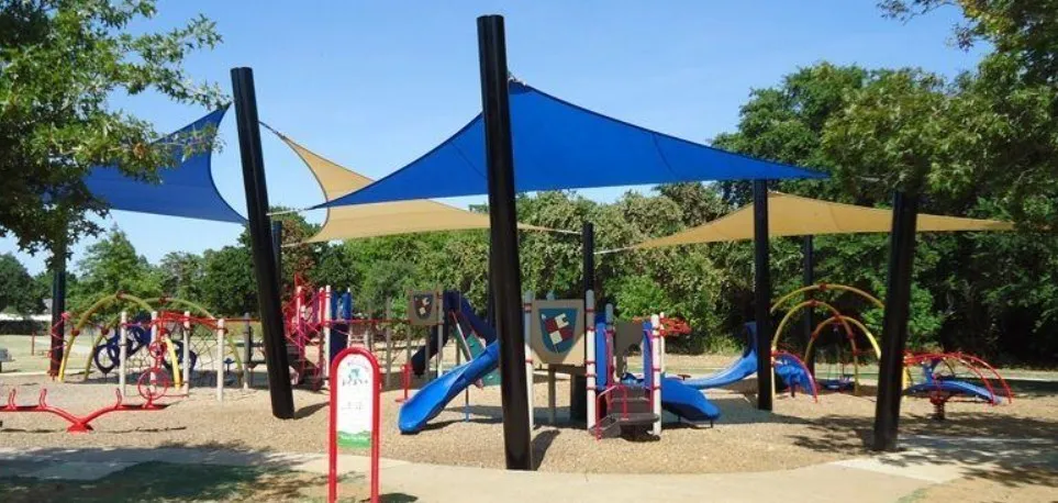 Outdoor play area featuring multiple shade structures, various play equipment, and a wood chip surface