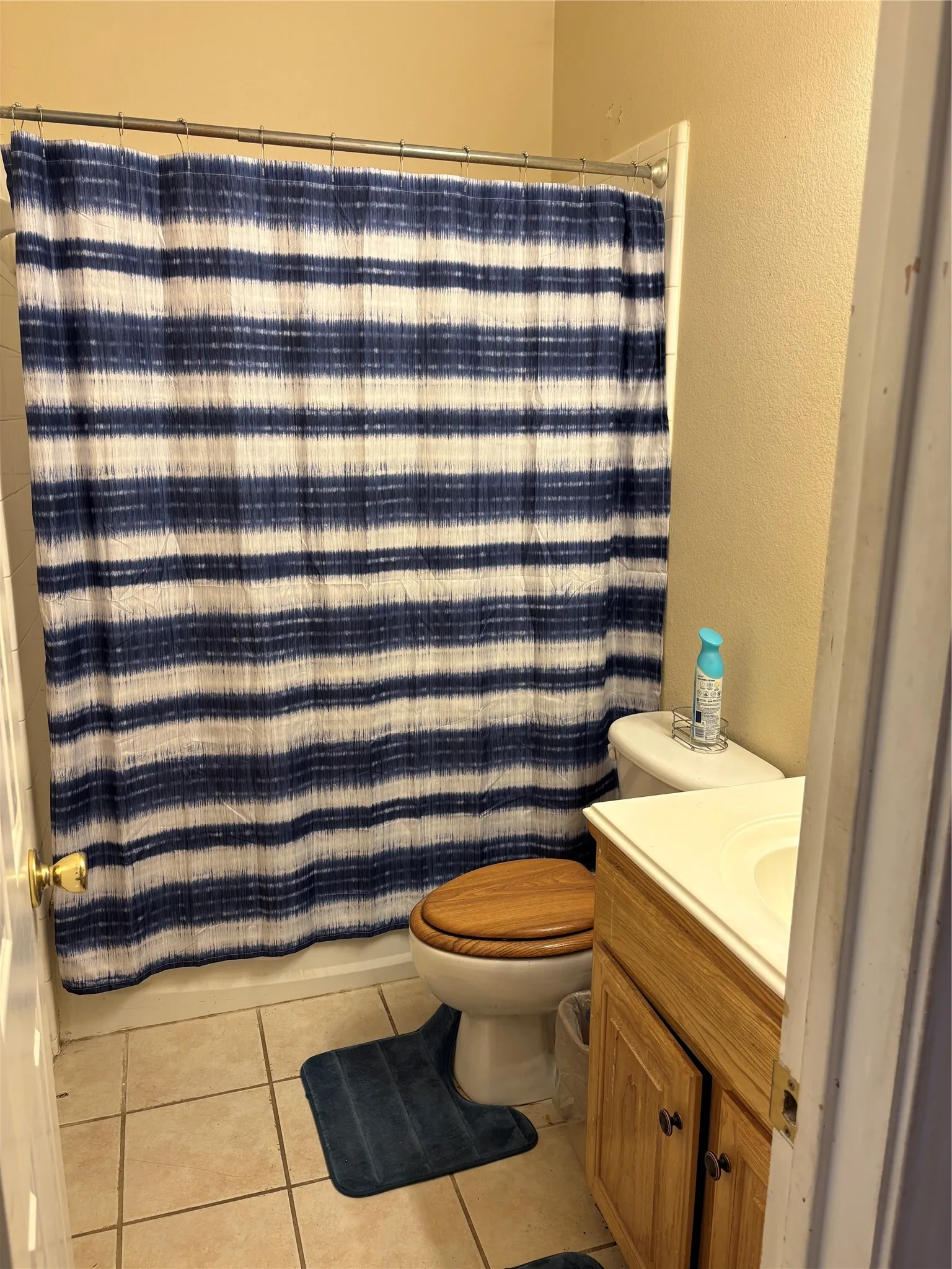 Neutral tone wall finish, ceramic tile flooring, wood-finish vanity with countertop sink, and a toilet with a wood-finish seat