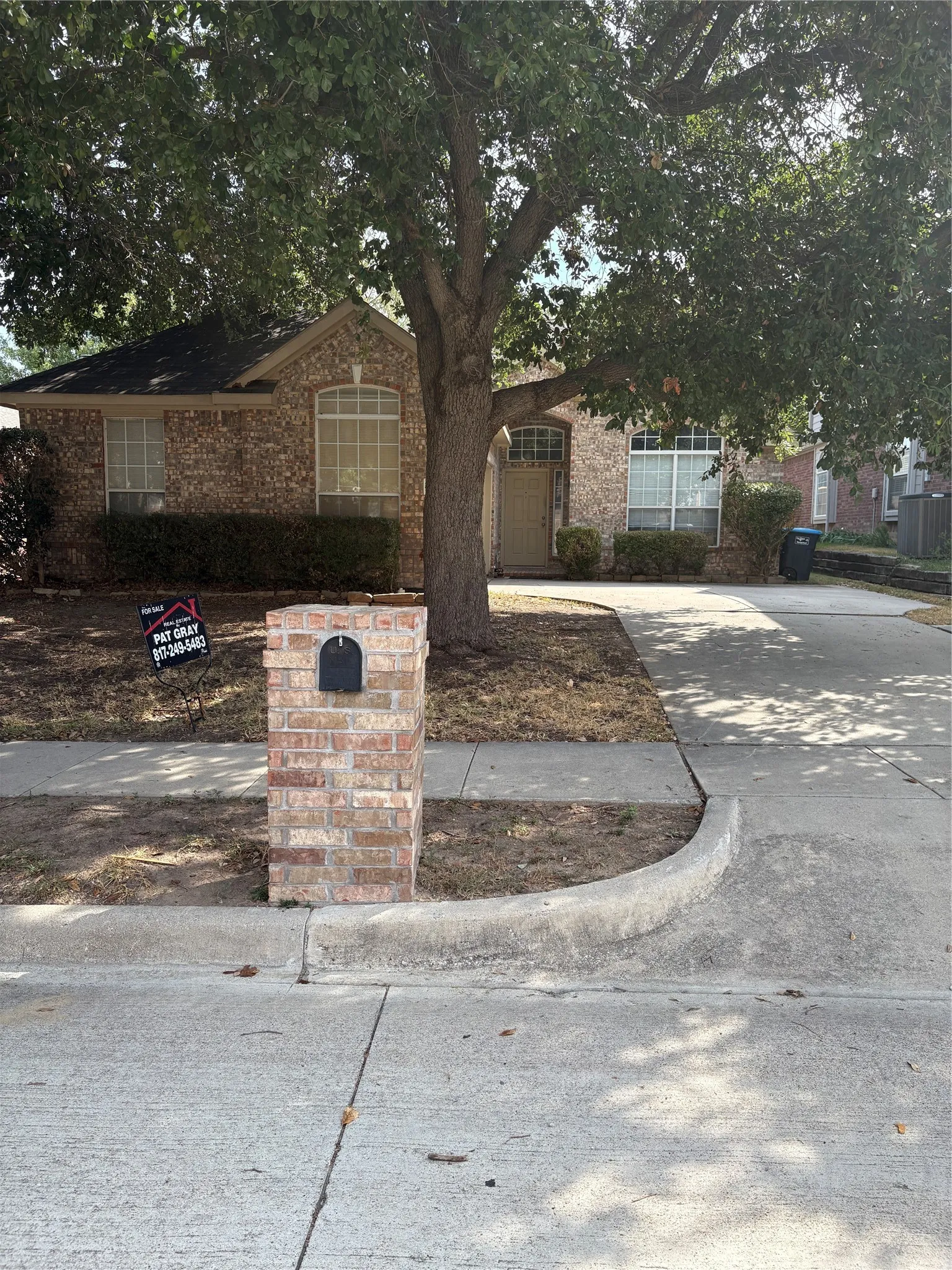 Brick facade, arched window detail, mature tree, concrete driveway, brick mailbox
