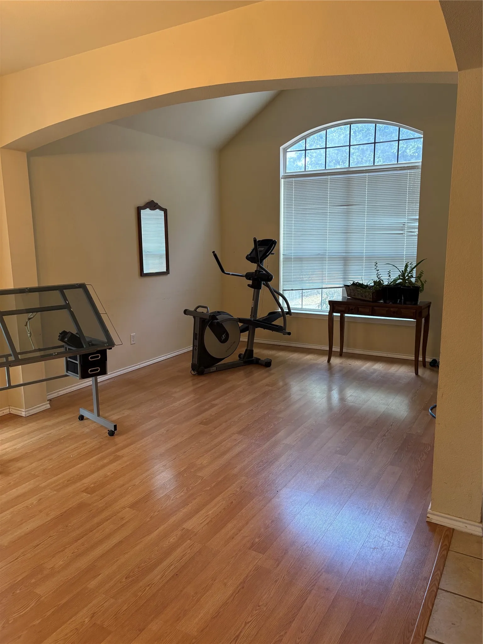 Wood-finish flooring throughout, arched entryway, vaulted ceiling, and an arched window