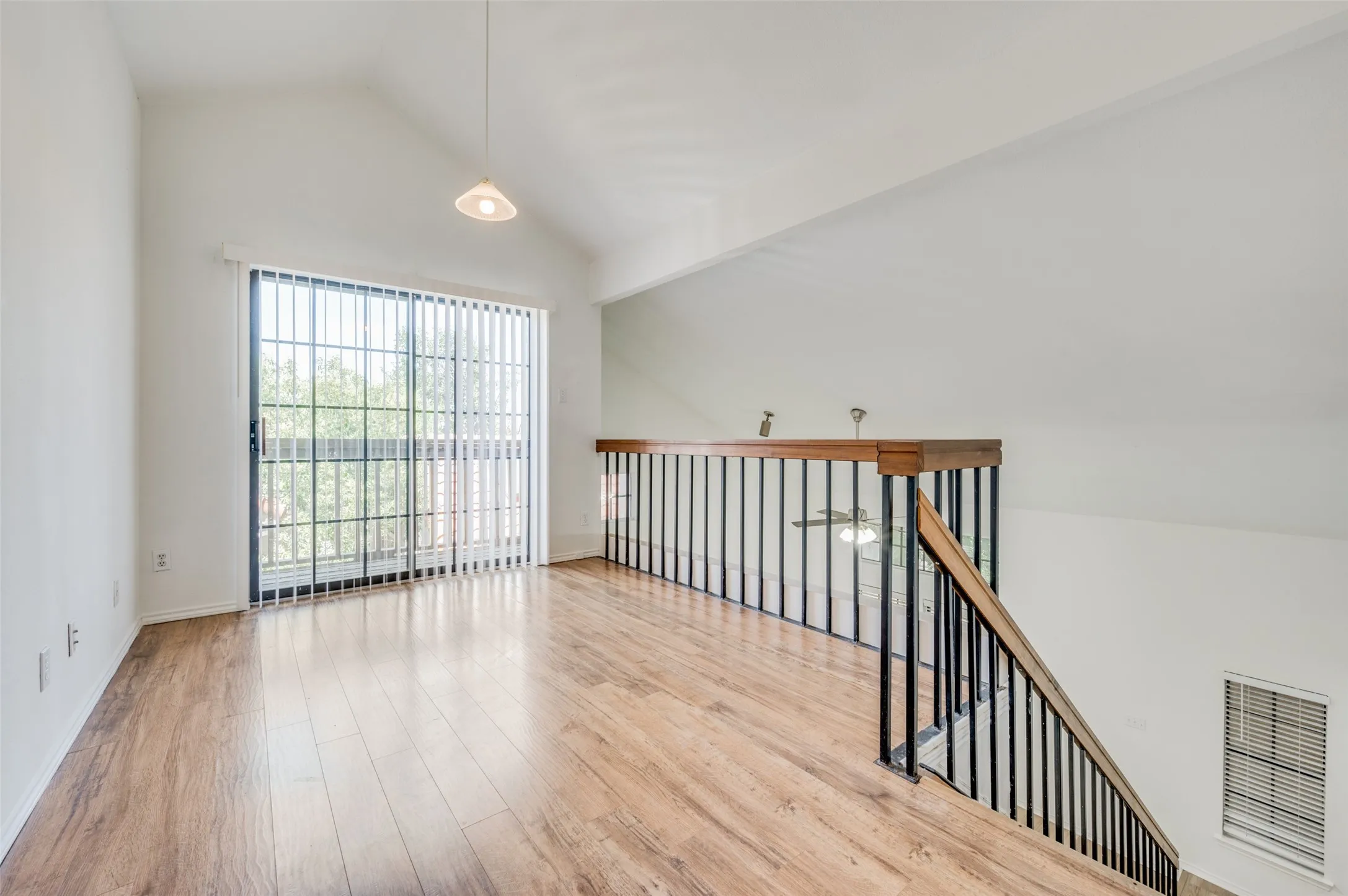 Open loft area featuring vaulted ceilings, wood-finish flooring, and a sliding glass door with vertical blinds