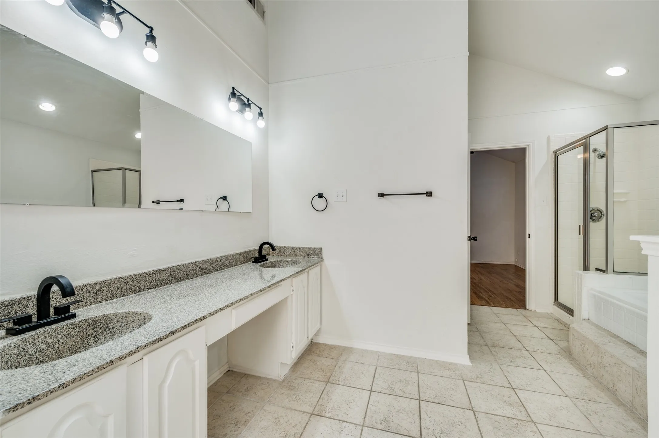 Spacious bathroom featuring a dual vanity with granite-style countertops and matte black fixtures