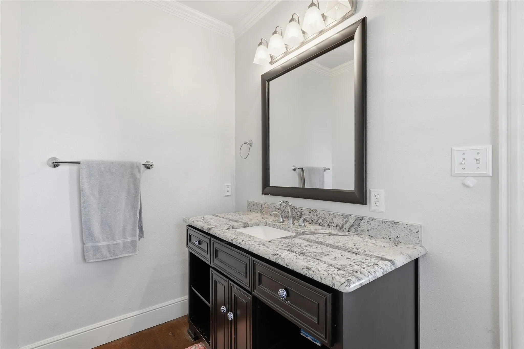 Single vanity featuring a granite countertop, undermount sink, and a dark wood-finish cabinet with decorative hardware