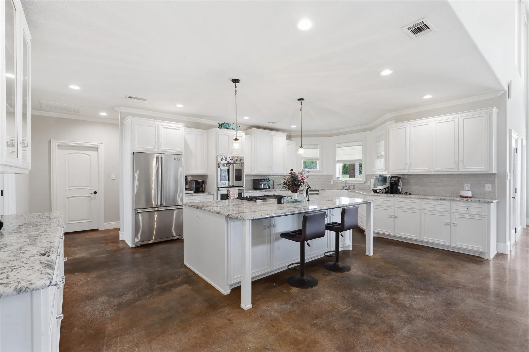 Spacious kitchen featuring an expansive center island with seating, extensive white cabinetry, durable concrete flooring, stainless steel appliances, and abundant recessed lighting