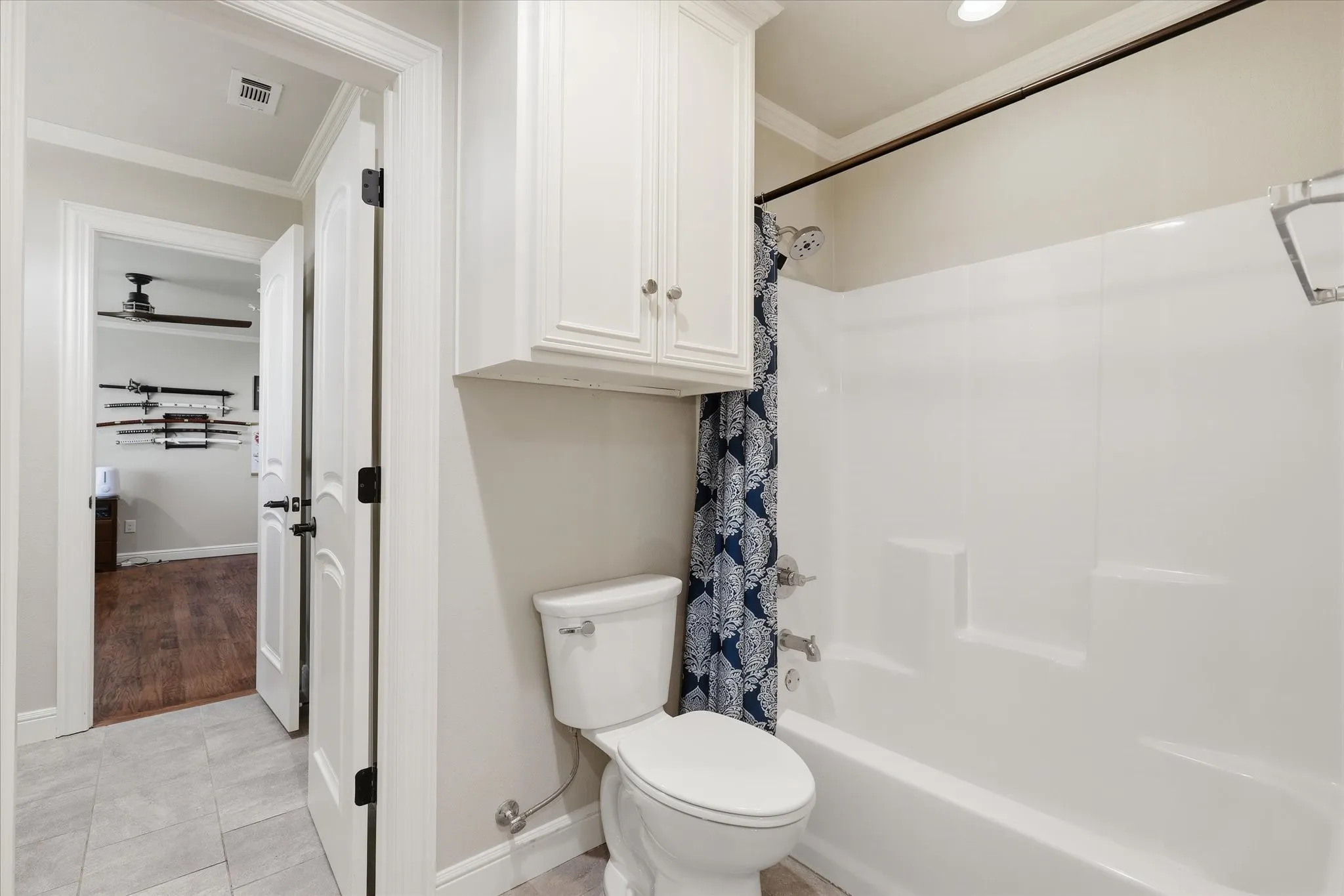 Bathroom featuring a white tub/shower combination, white toilet, and white upper cabinetry