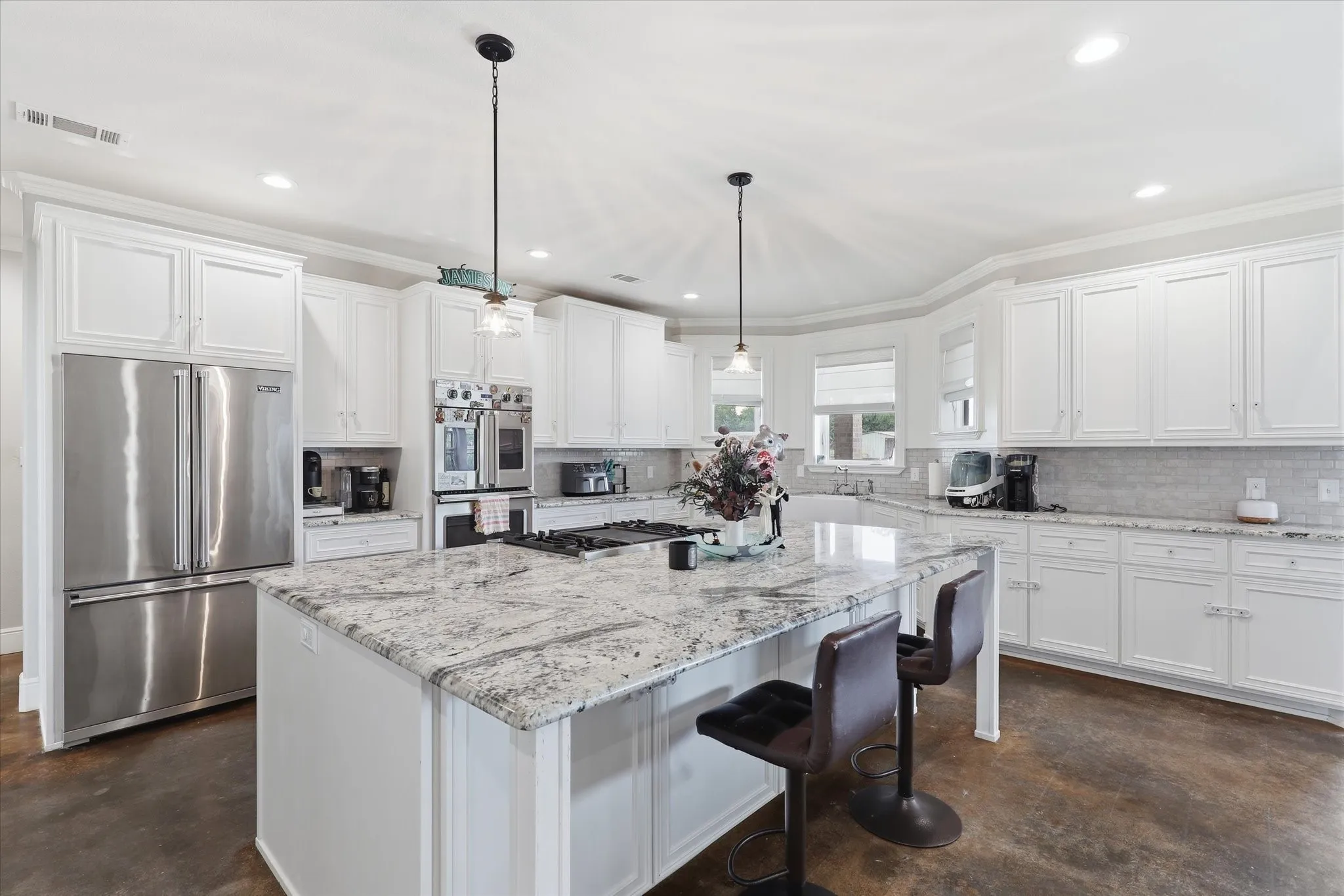 Spacious kitchen featuring an expansive central island with a light-toned countertop, white cabinetry, a built-in double oven, and recessed lighting