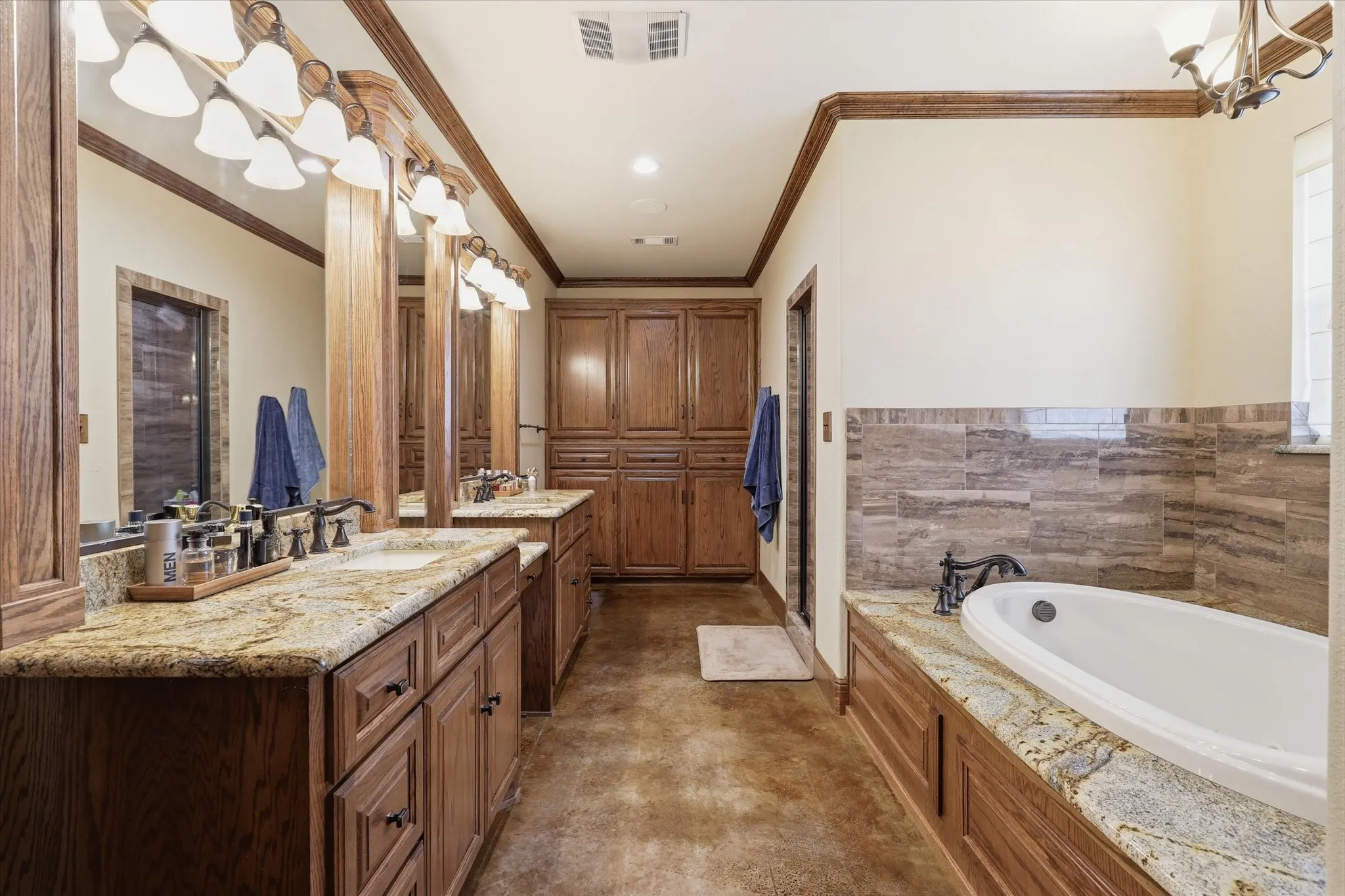 Spacious bathroom featuring a built-in soaking tub, dual vanity with granite countertops, wood-finish cabinetry, and full-height built-in storage