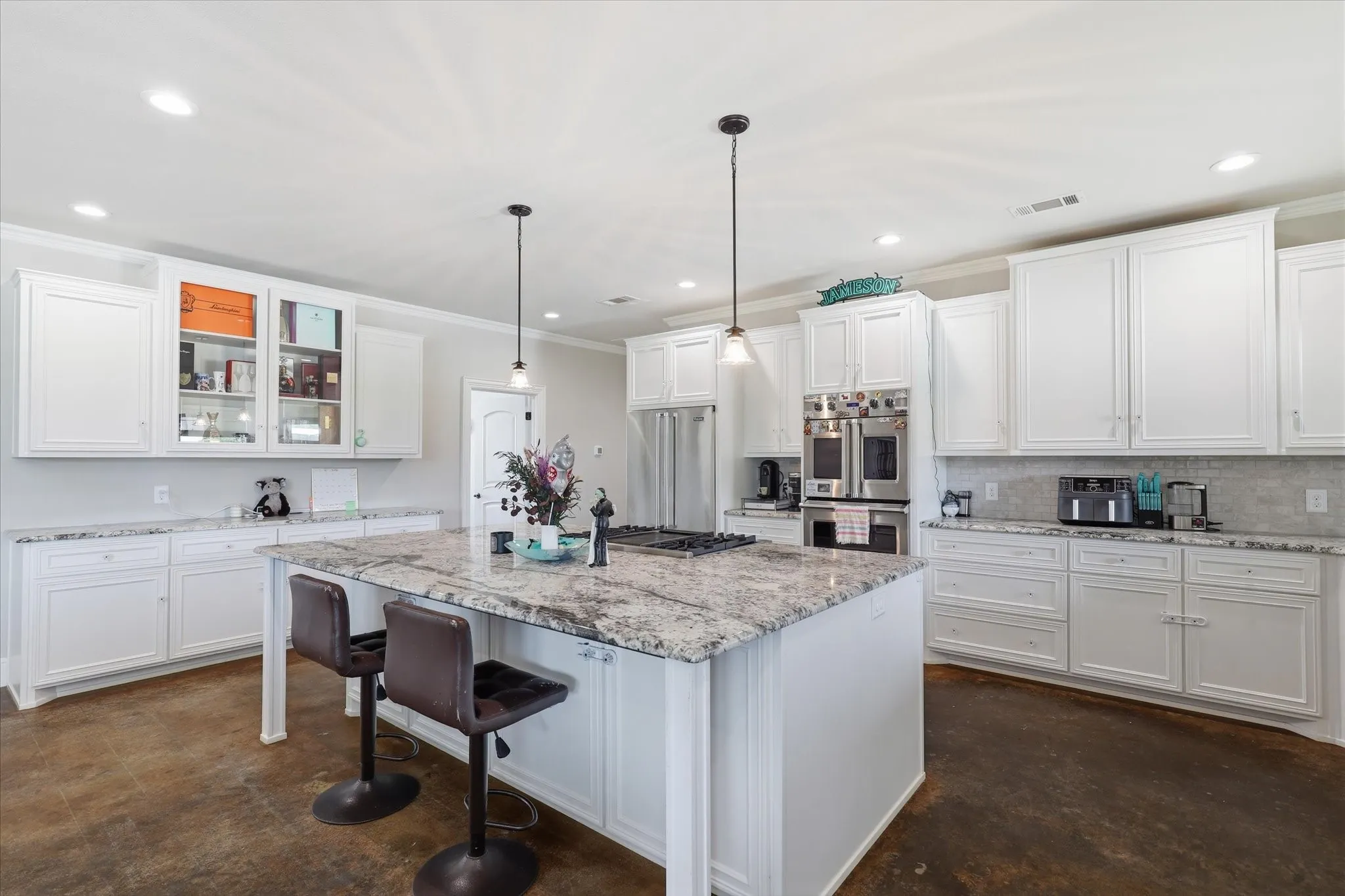 Spacious kitchen featuring an expansive center island with seating, ample white cabinetry, stone countertops, a tile backsplash, and stainless steel double ovens