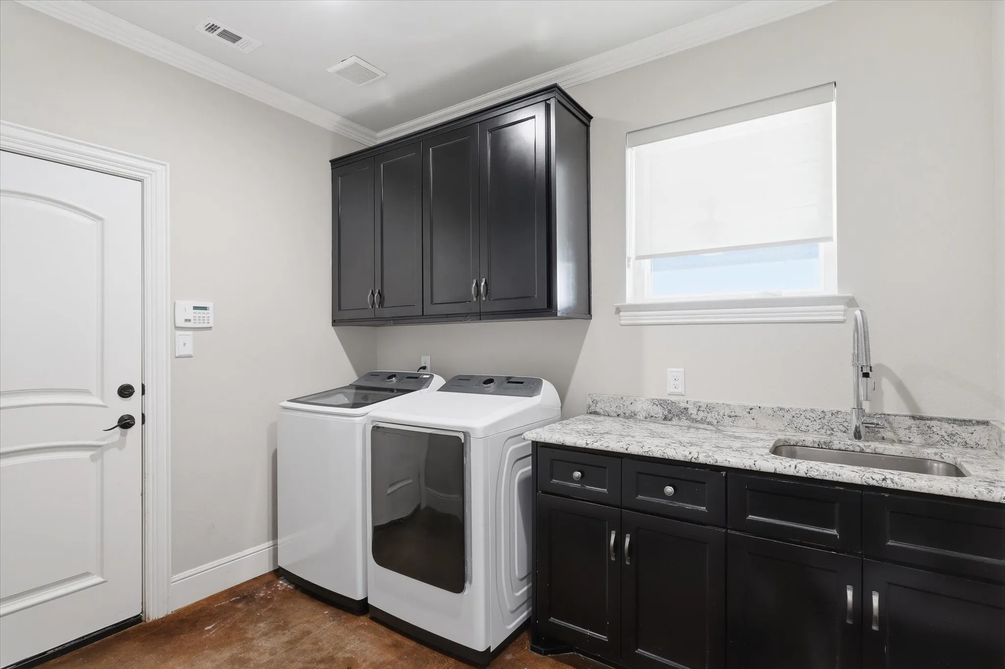 Laundry room featuring dark wood-finish cabinetry, granite-style countertop with an undermount sink, and a window with a roller shade