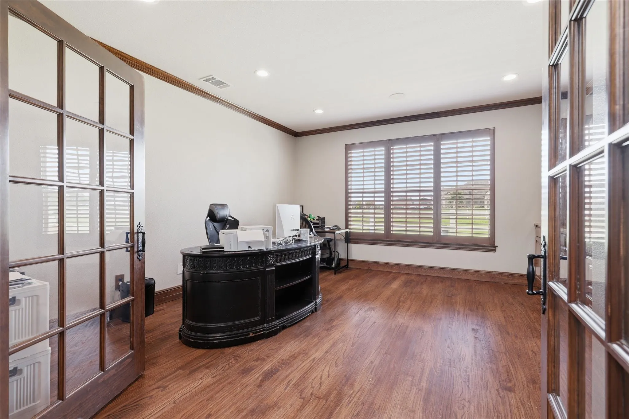Double French doors open to a room featuring wood-finish flooring, plantation shutters, recessed lighting, and crown molding
