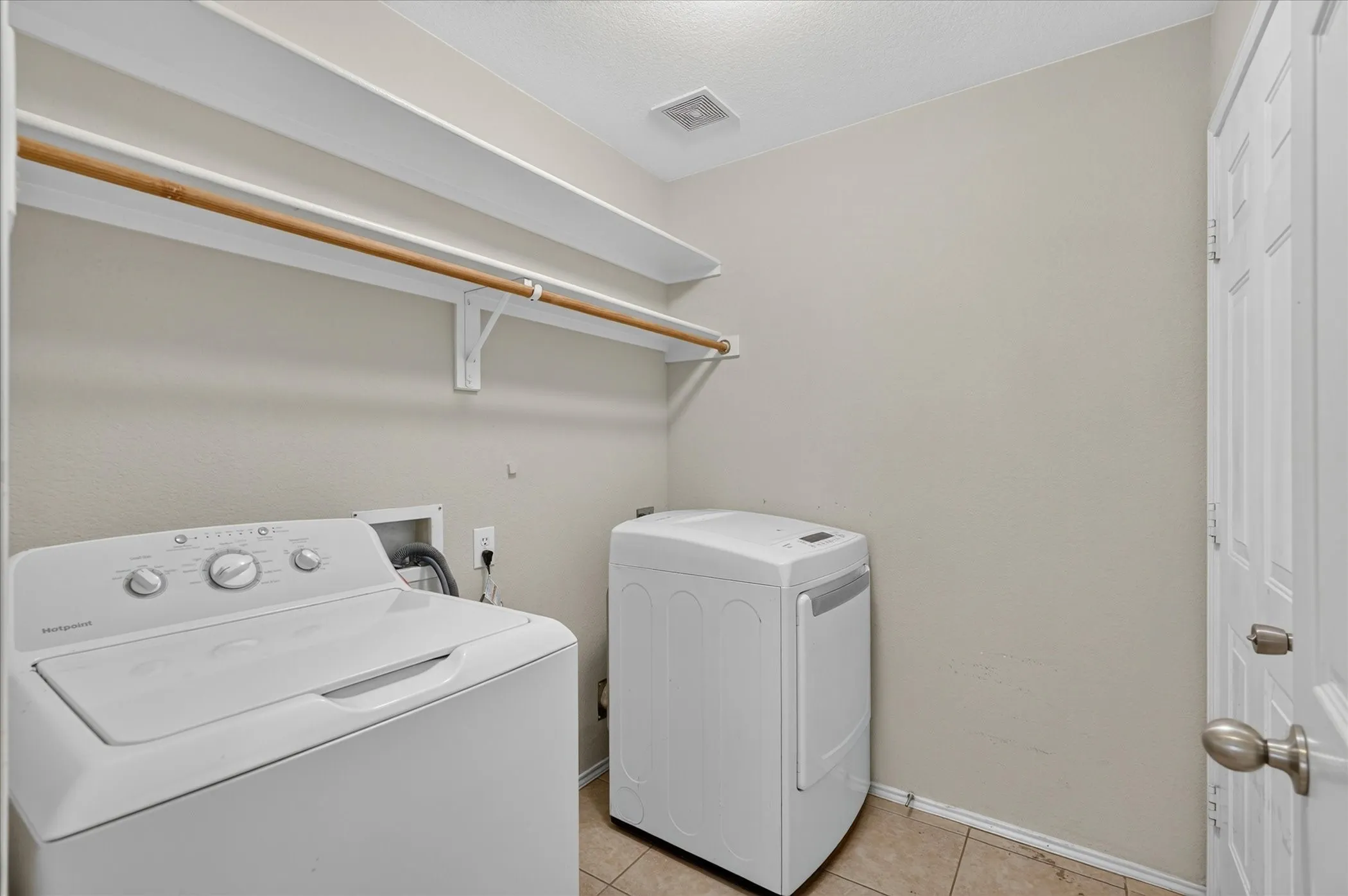 Dedicated utility room featuring tile flooring, neutral wall tones, and built-in shelving with a hanging rod