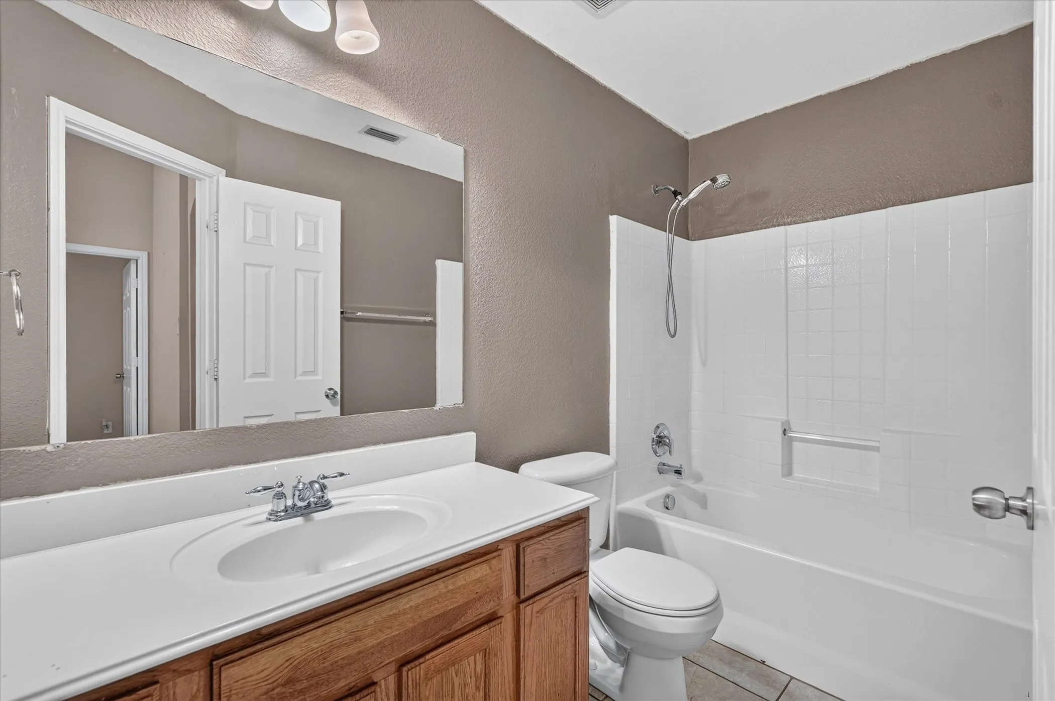 Bathroom featuring a wood-finish vanity with an integrated sink, a large wall-mounted mirror, a tub and shower combination with white tile surround, and neutral-toned wall paint