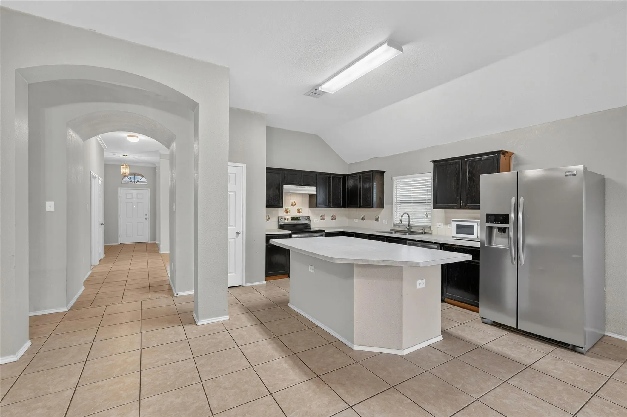 Kitchen featuring a center island with a light-toned countertop, dark wood-finish cabinetry, stainless steel appliances, and tile flooring