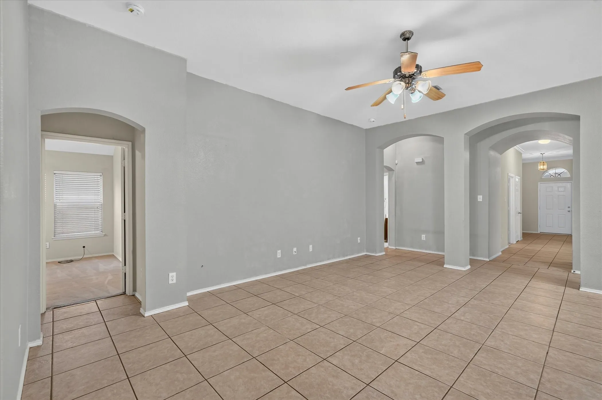 Spacious living area featuring neutral-toned tile flooring, vaulted ceilings, and a ceiling fan with integrated lighting