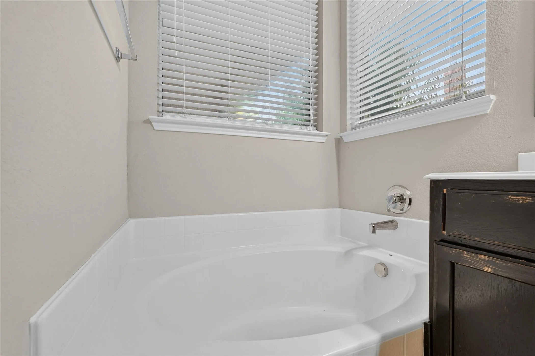 Corner soaking tub with polished chrome fixtures and two windows featuring blinds
