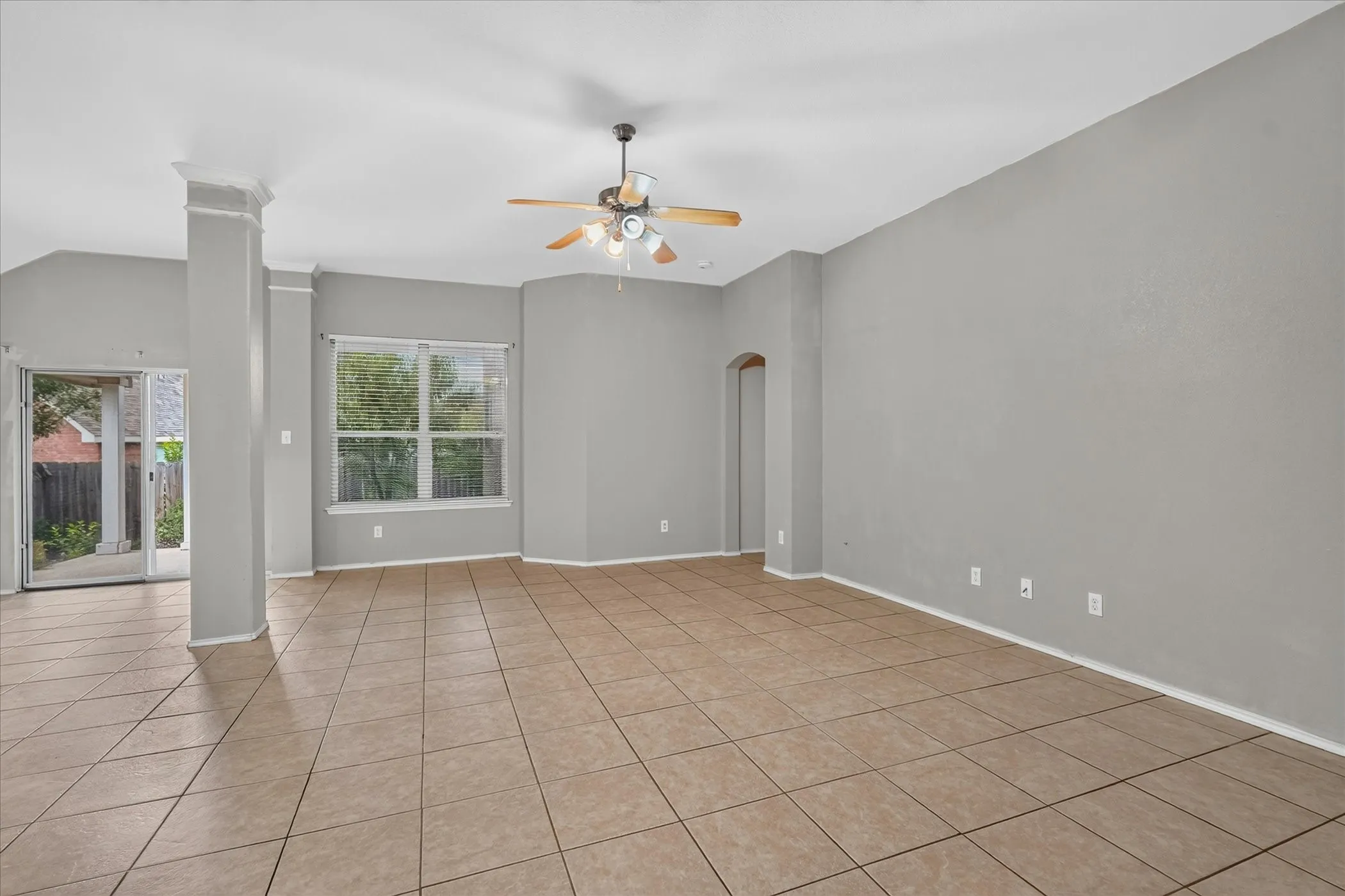 Spacious interior room featuring neutral gray walls, light-toned tile flooring, and a ceiling fan with integrated lighting