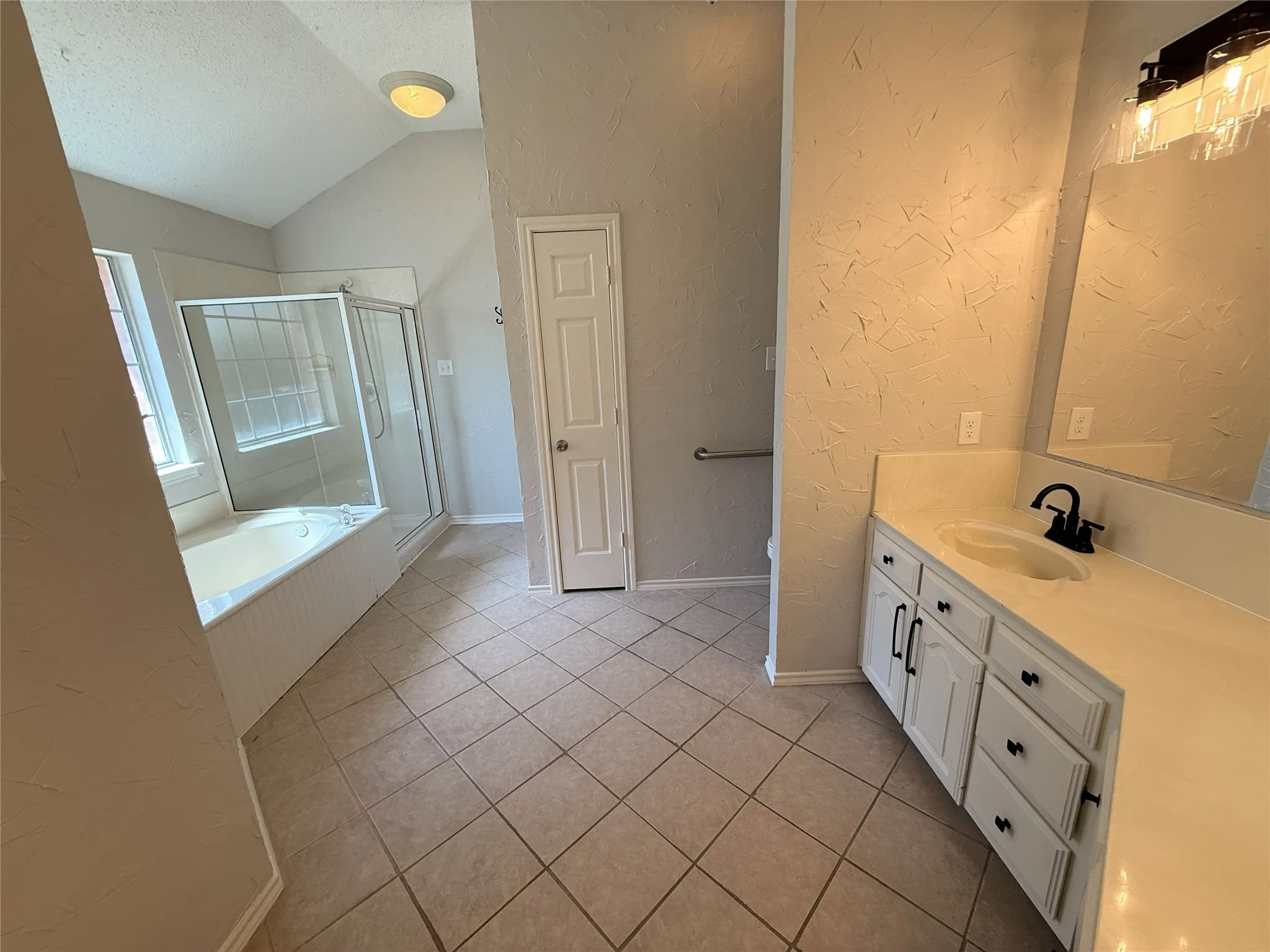 Bathroom featuring a tiled floor, double vanity with white cabinetry, built-in bathtub, and a separate glass-enclosed shower