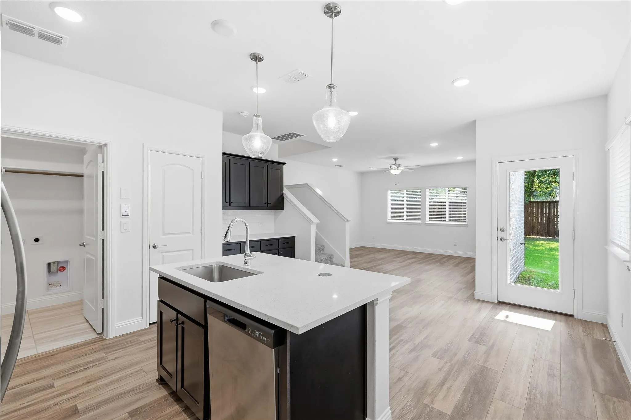 Open-concept kitchen featuring a central island with an undermount sink and dishwasher, quartz countertops, pendant lighting, and wood-finish flooring
