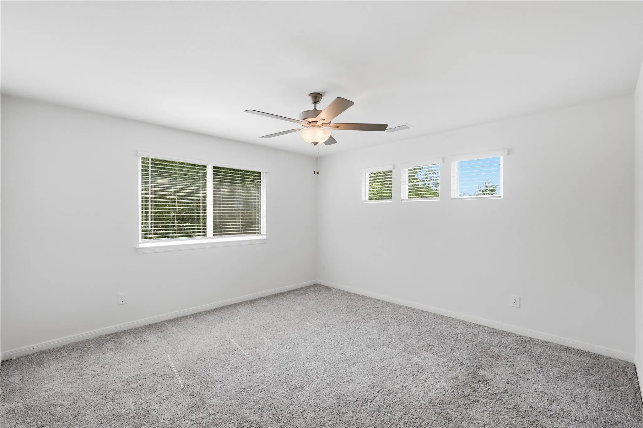 Bright and spacious bedroom offering neutral carpeting, abundant natural light from multiple windows, and a ceiling fan with integrated lighting fixture
