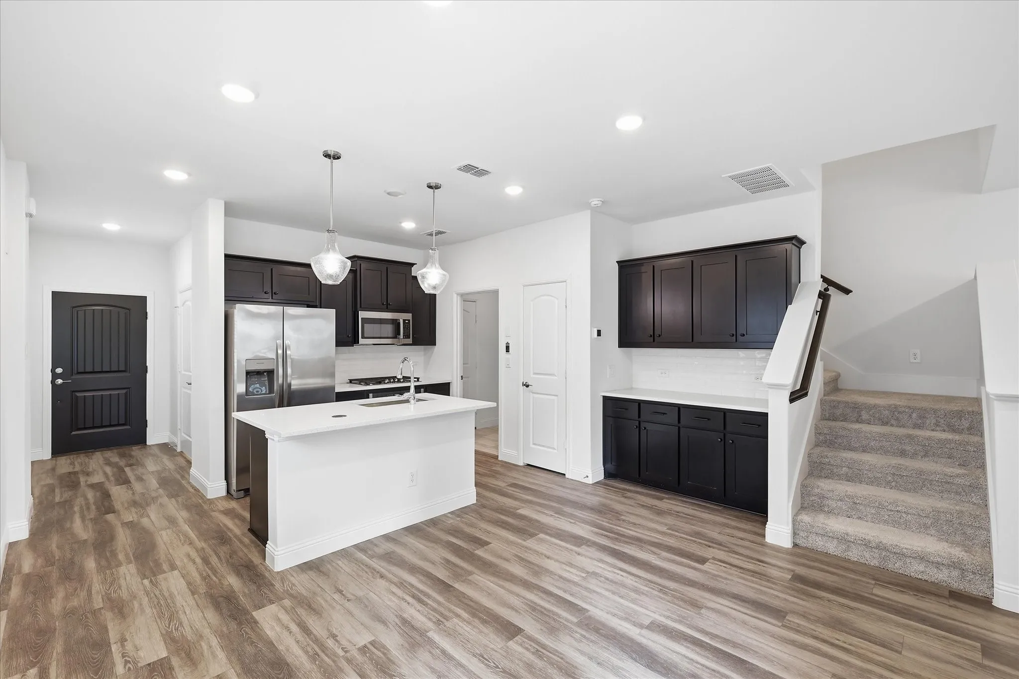 Open-concept living space with wood-finish flooring, a kitchen island, dark cabinetry, stainless steel appliances, and recessed lighting