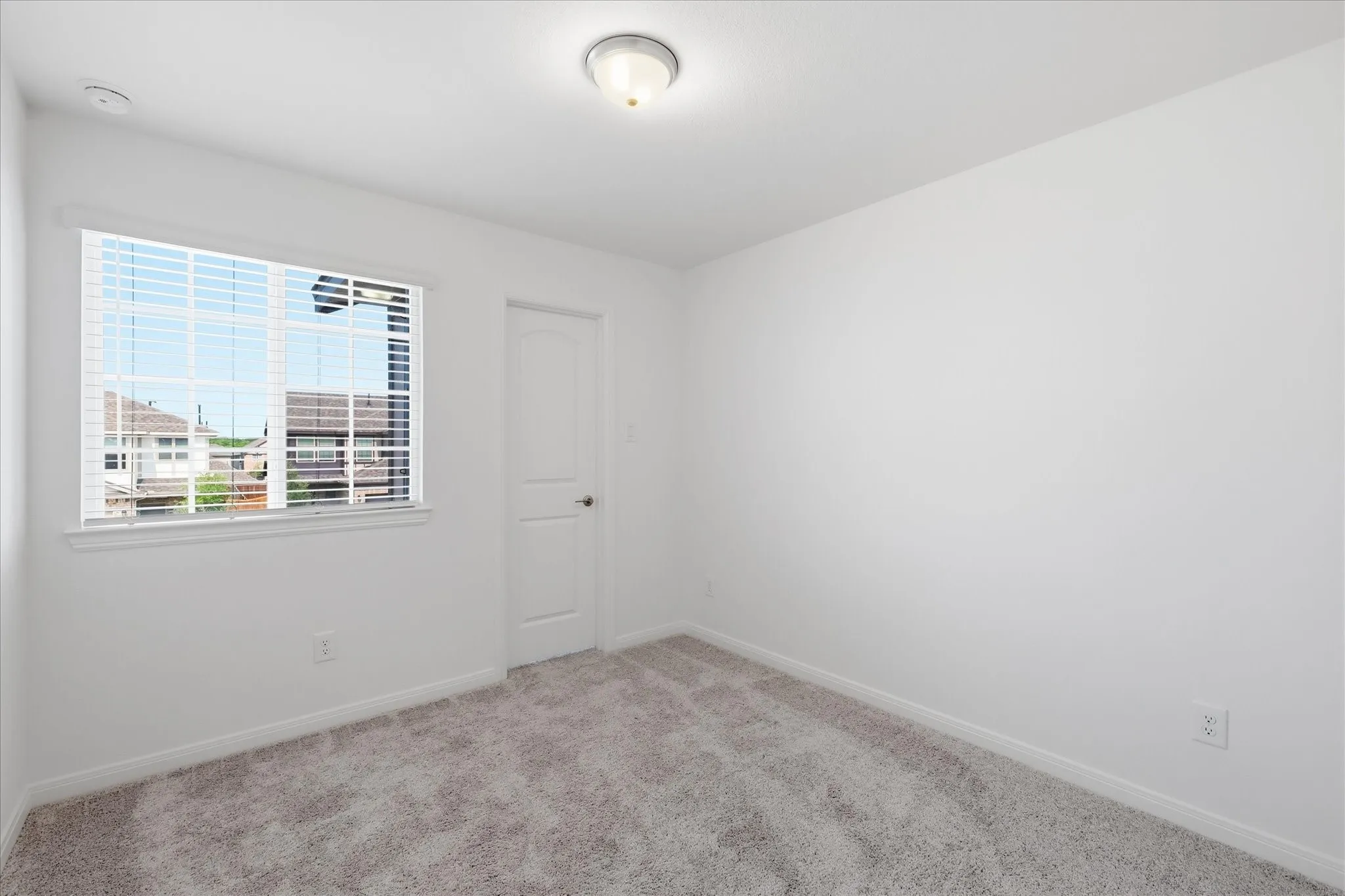 Bright bedroom with expansive window featuring city skyline views, neutral carpet flooring, and soft overhead lighting