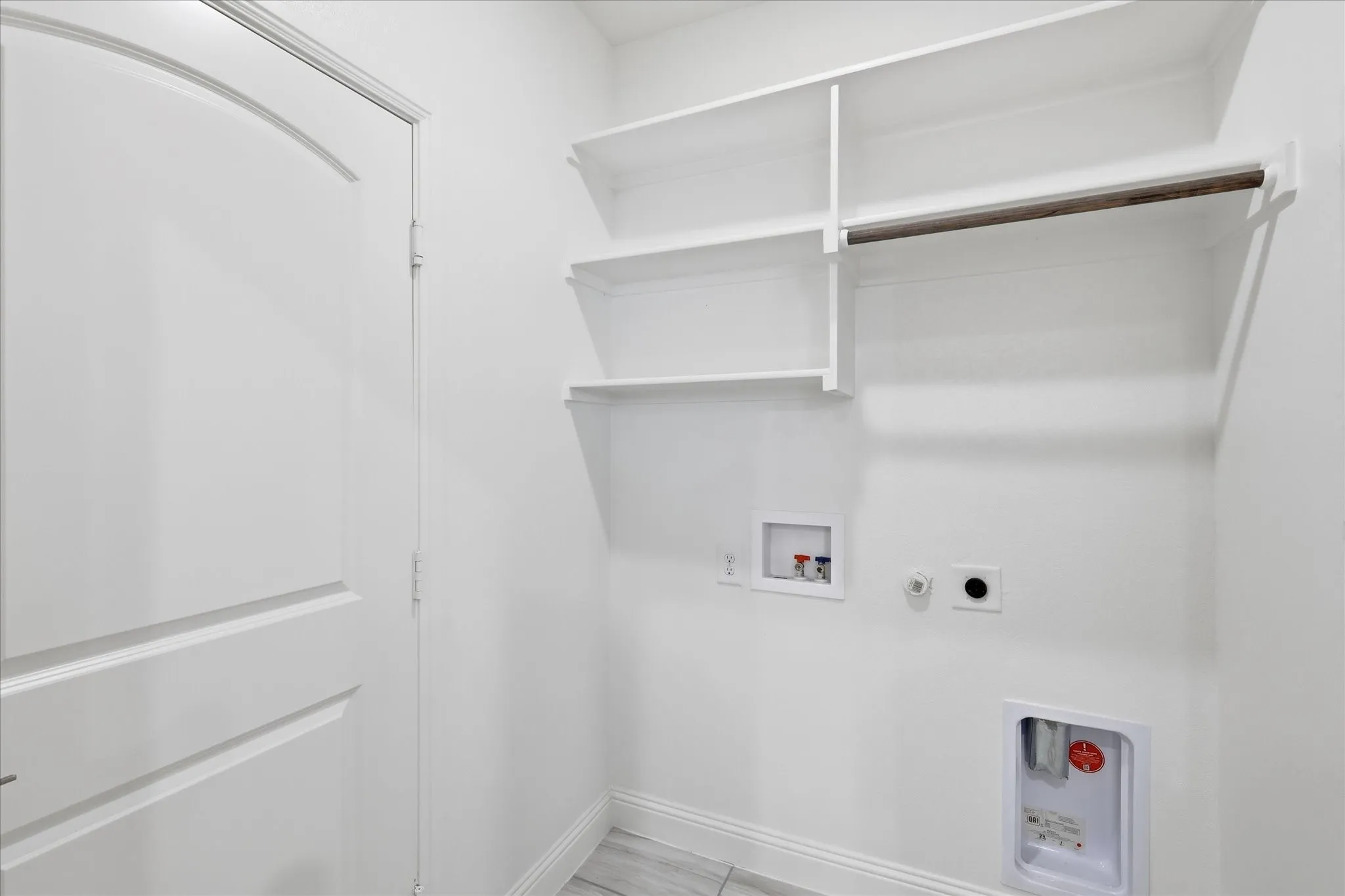 Utility closet featuring white shelving with multiple storage tiers, chrome rod for hanging, and integrated electrical outlets for convenient access to mechanical systems and storage solutions