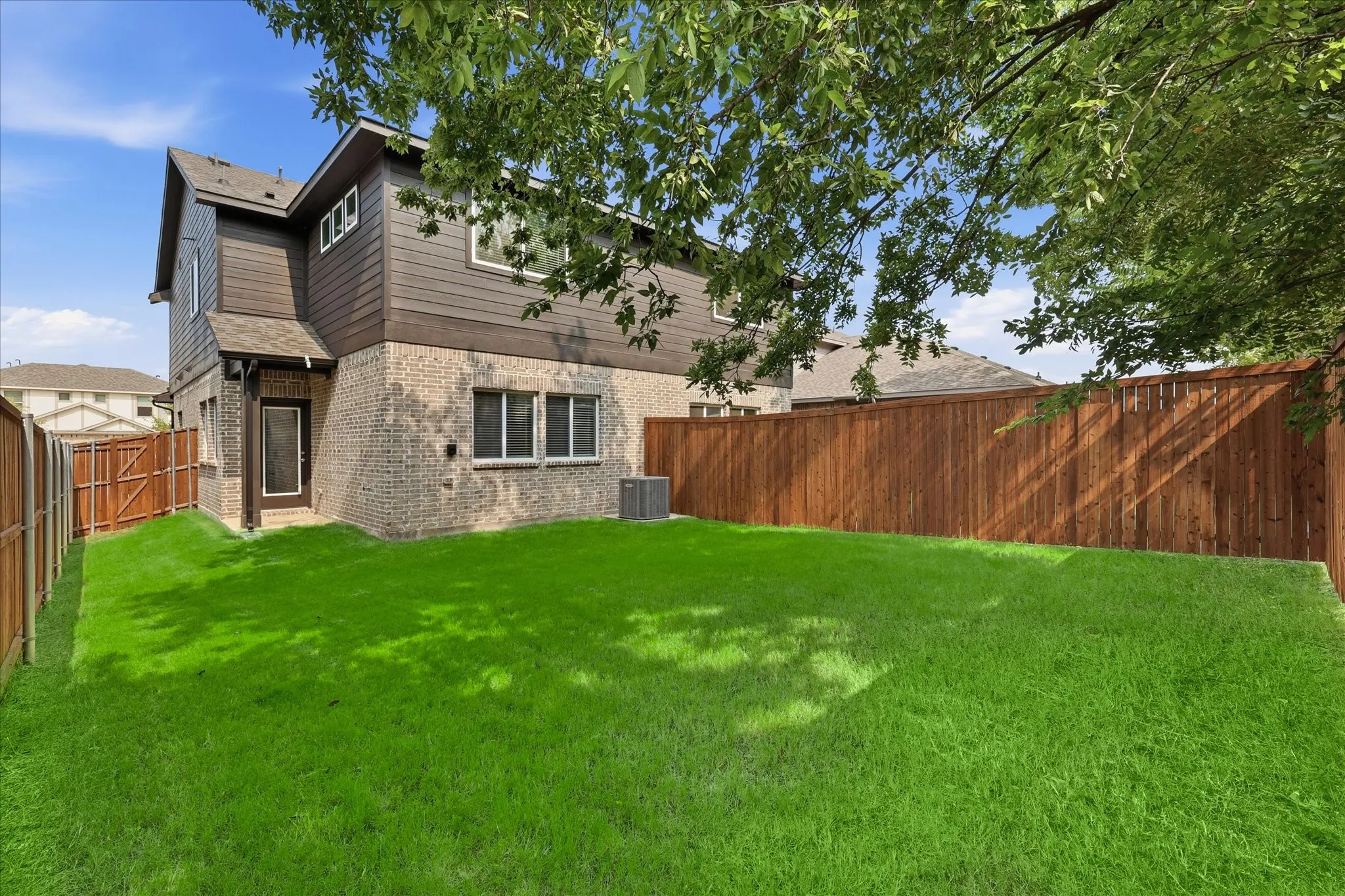 Expansive backyard featuring a lush, manicured lawn with mature tree coverage providing natural shade
