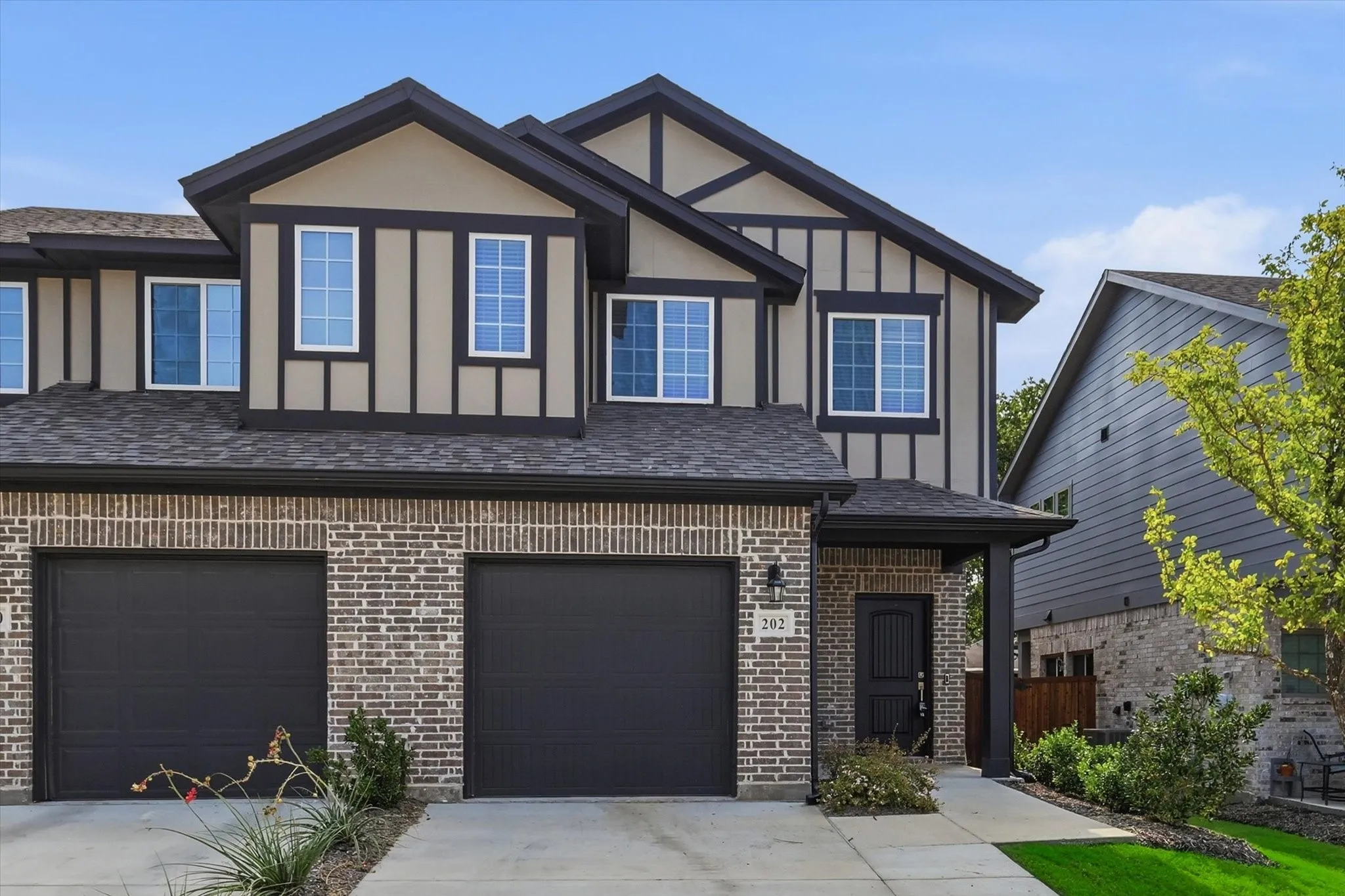 Modern Tudor-style facade featuring two garage bays with dark doors, a covered entryway, and second-story windows