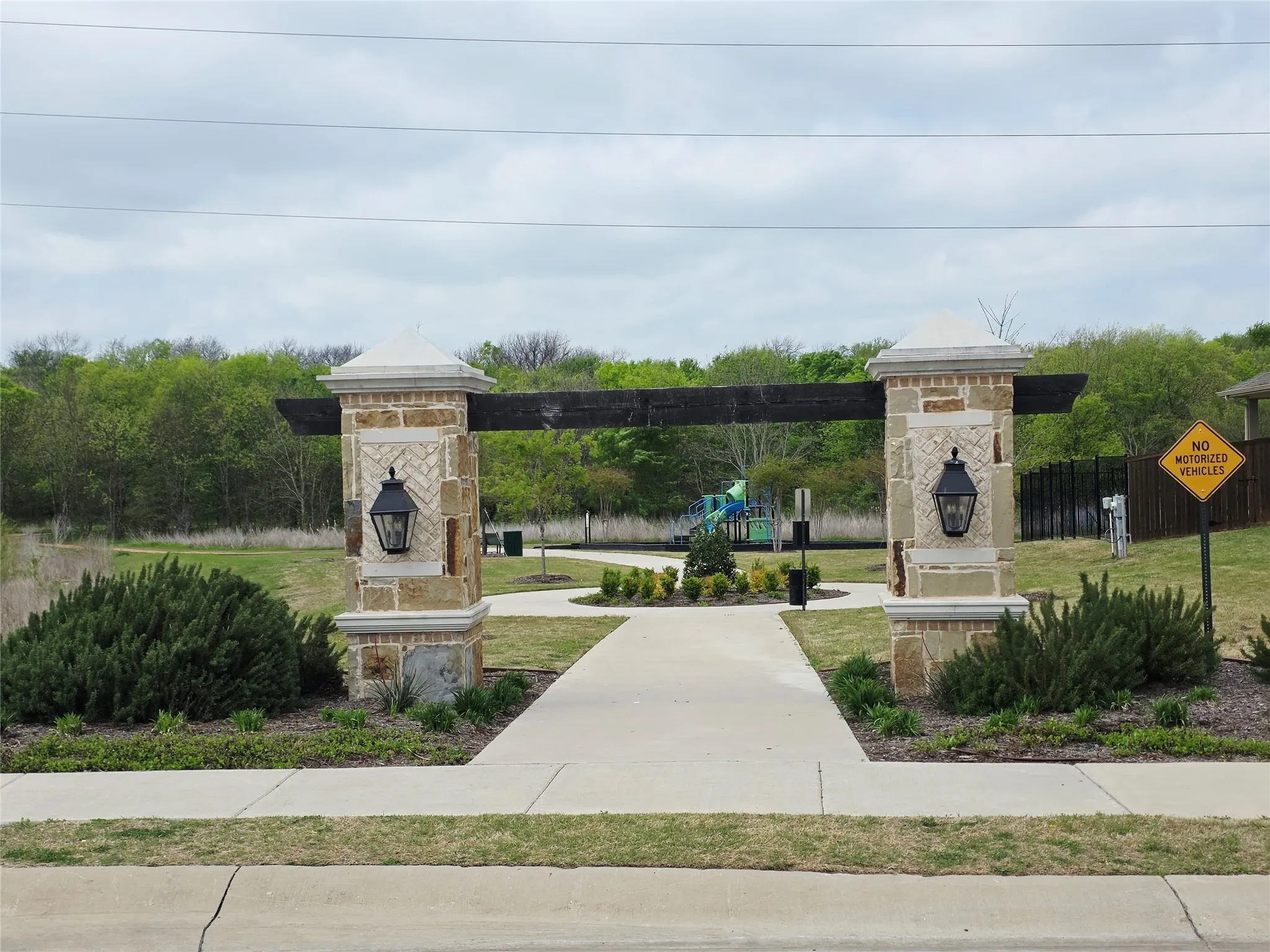 Stone and wood-beam archway entrance featuring integrated lighting, concrete walkway, and landscaped shrubbery