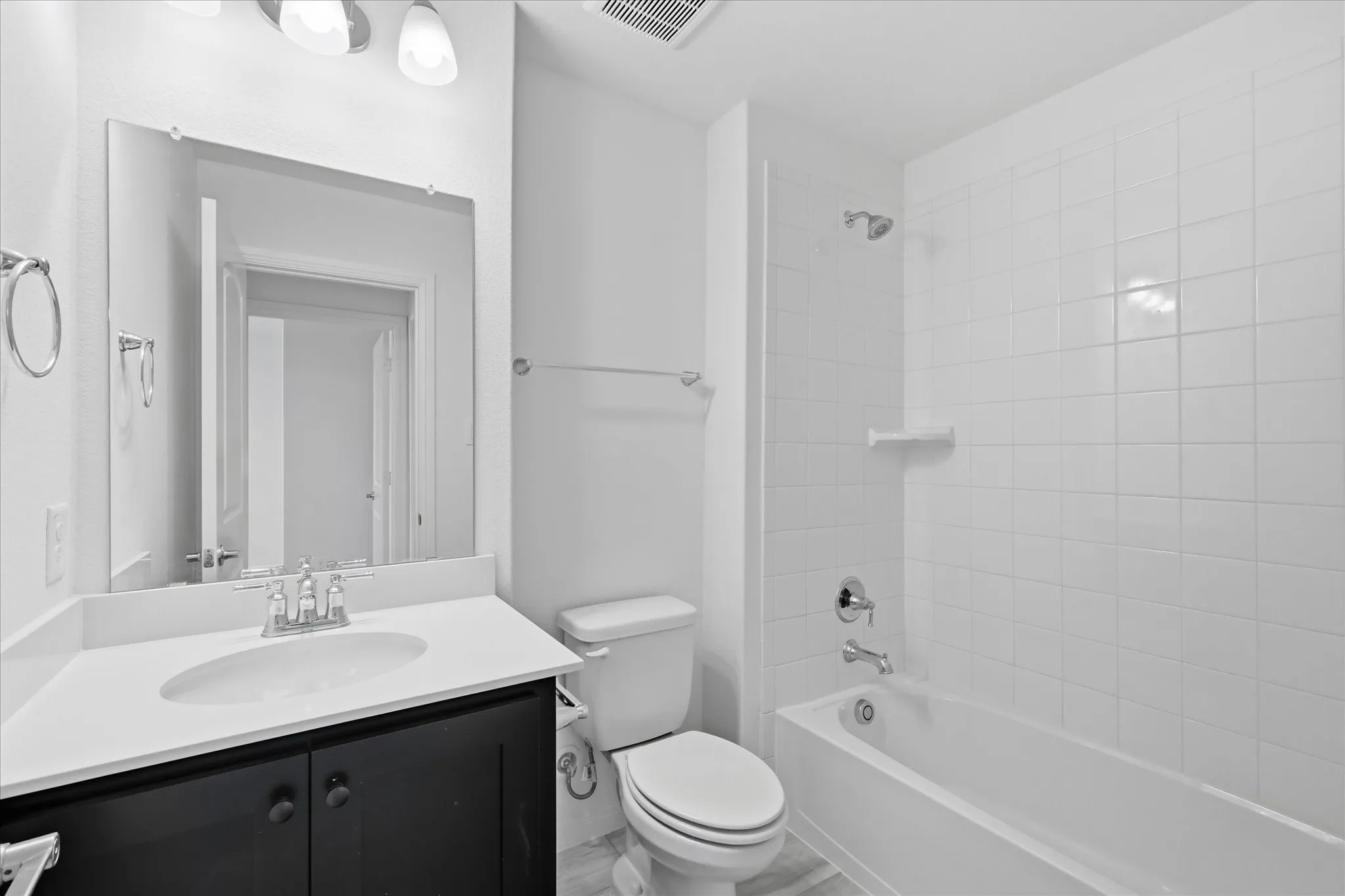 Bathroom featuring a vanity with dark cabinetry and white countertop, an undermount sink, a large wall-mounted mirror, a toilet, and a shower-over-tub with white subway tile surround
