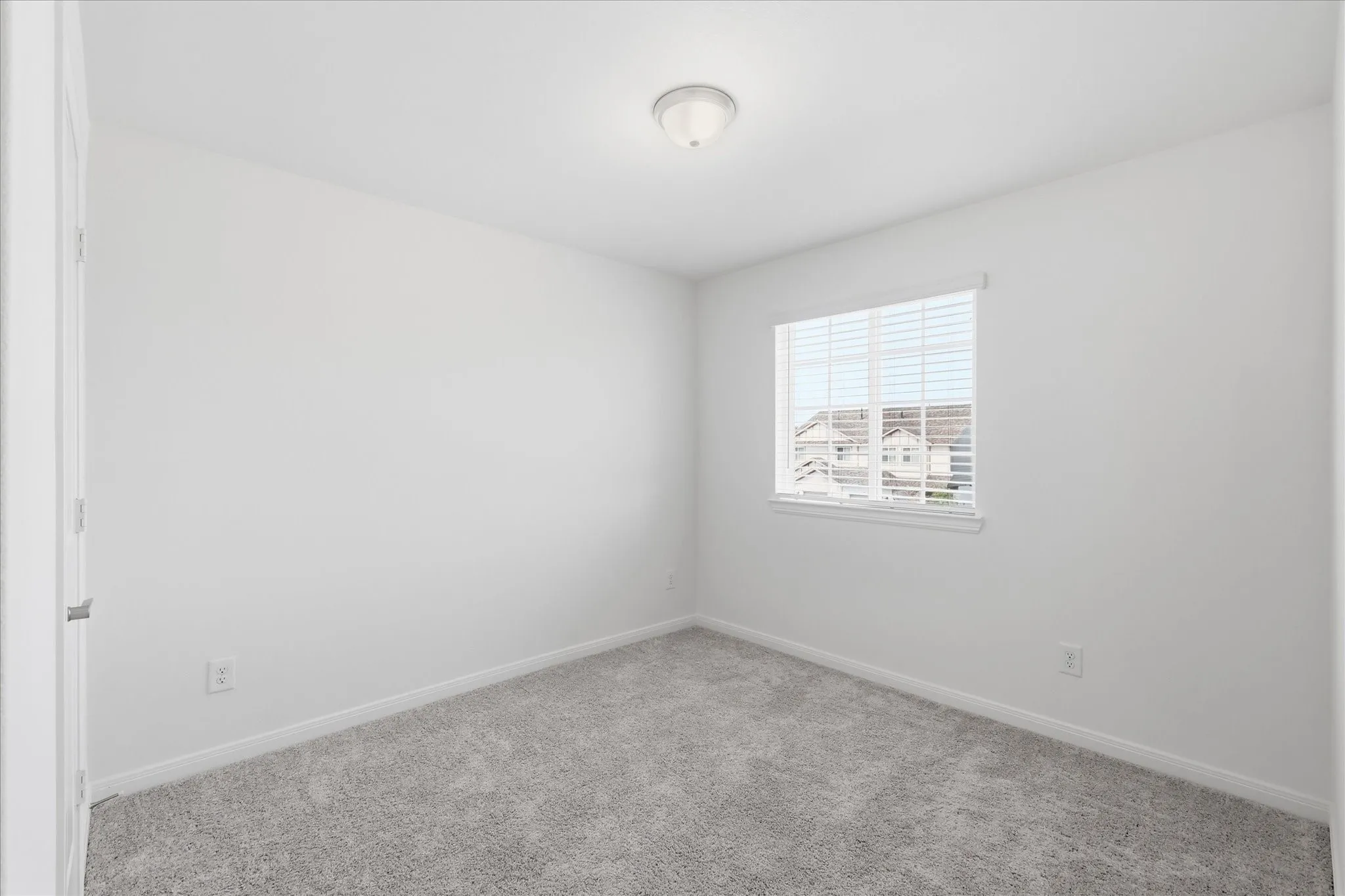 Bright secondary bedroom featuring neutral wall finishes, carpet flooring, and a large casement window with plantation shutters allowing abundant natural light