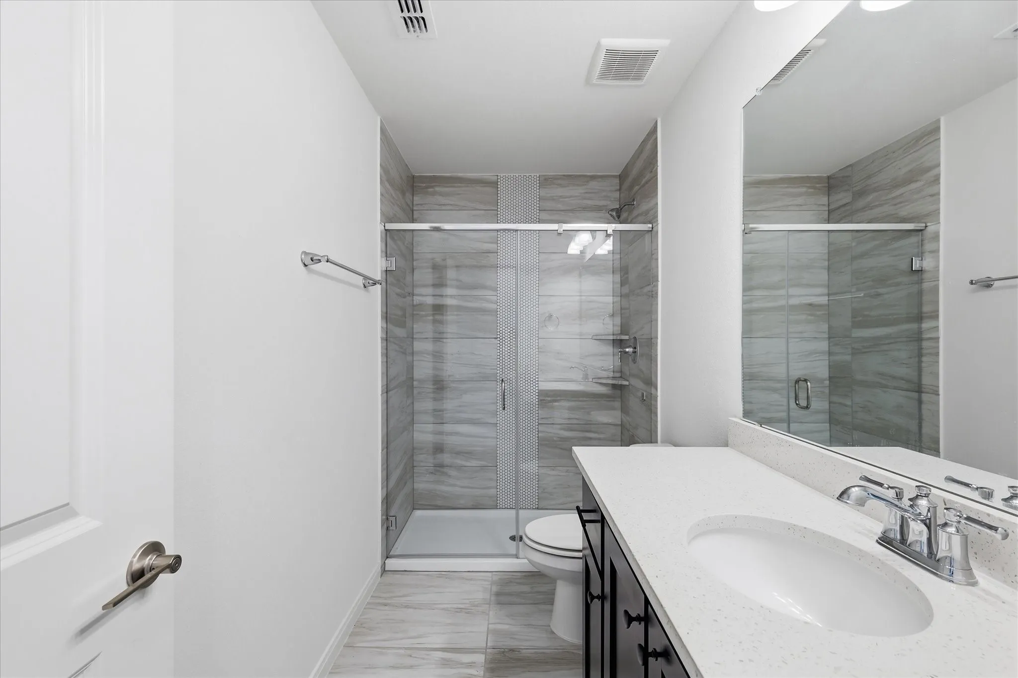 Spa-inspired primary bathroom featuring a frameless glass-enclosed walk-in shower with horizontal linear tile detailing, dual vanity with undermount sink and chrome fixtures, quartz countertop, and wood-finish flooring throughout