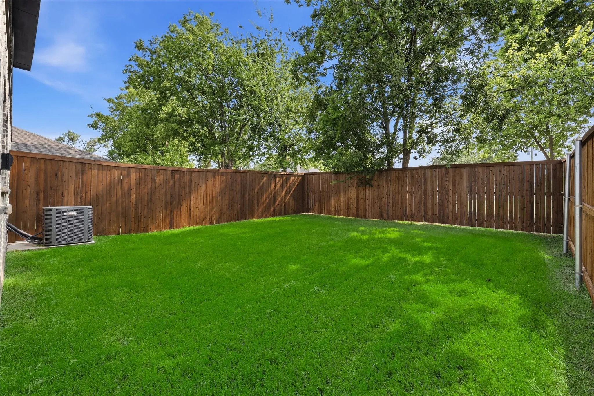 Expansive backyard featuring a lush, manicured lawn bordered by mature trees and wood-finish fencing