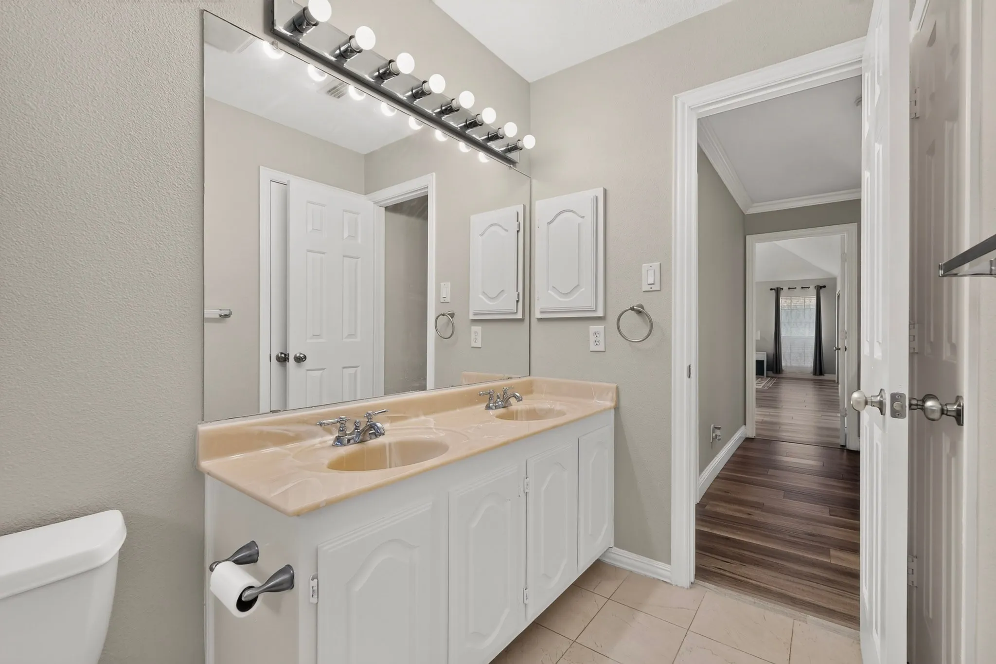 Bathroom featuring a dual vanity with a light-toned countertop, white cabinetry, and a large wall-mounted mirror with vanity lighting