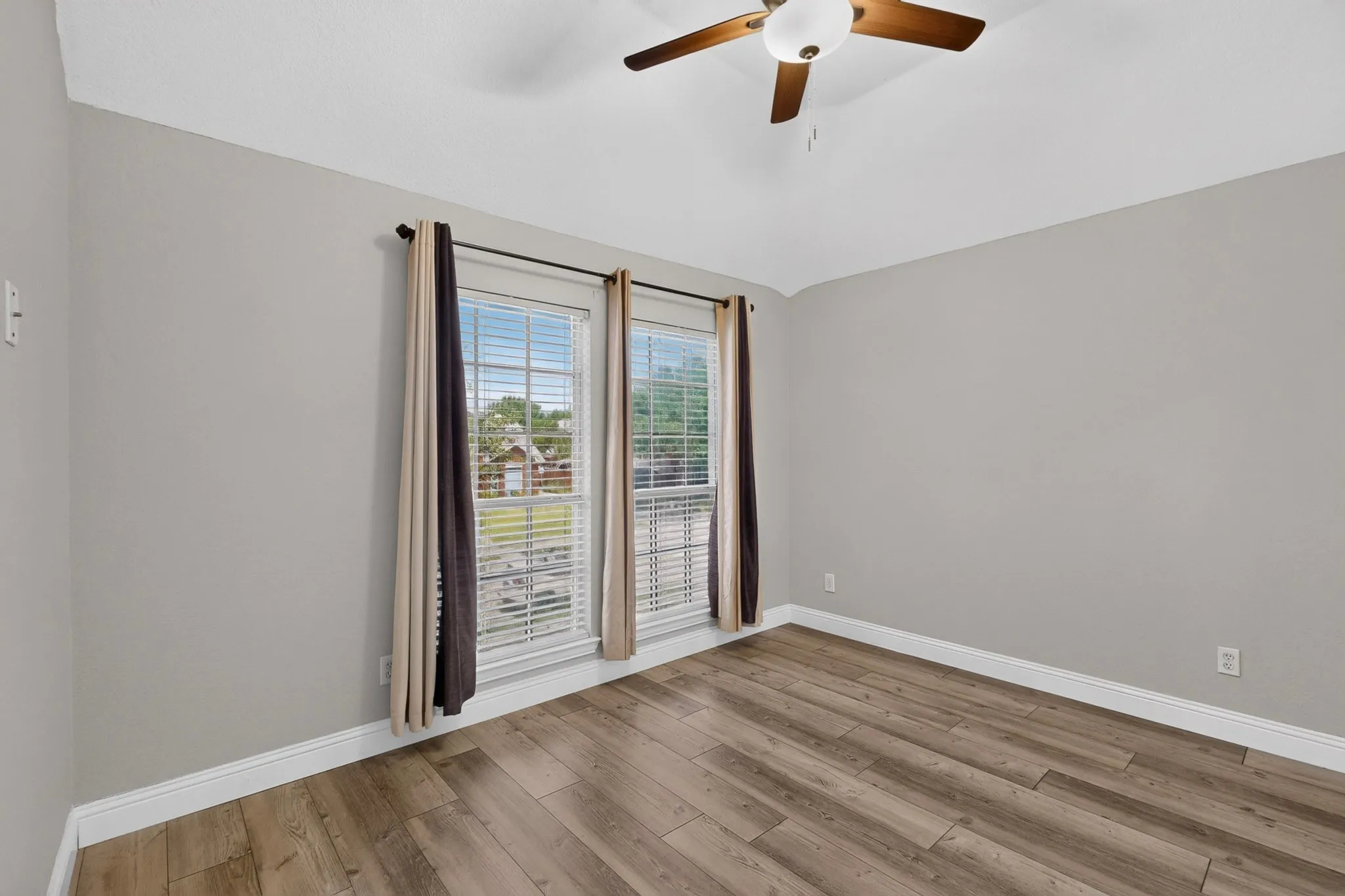 Spacious room featuring wood-finish flooring, light grey walls, and a vaulted ceiling with a ceiling fan