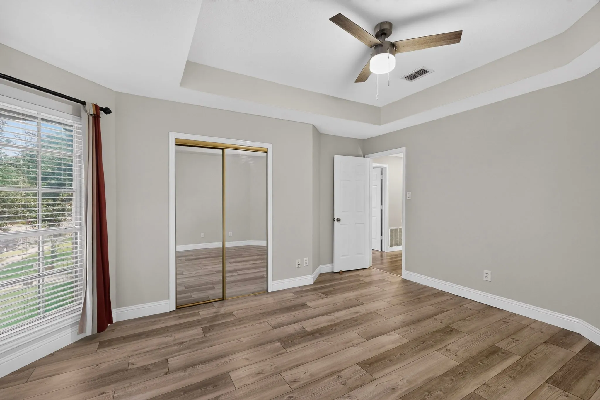 Spacious room featuring wood-finish flooring, a tray ceiling with a ceiling fan, and white baseboards
