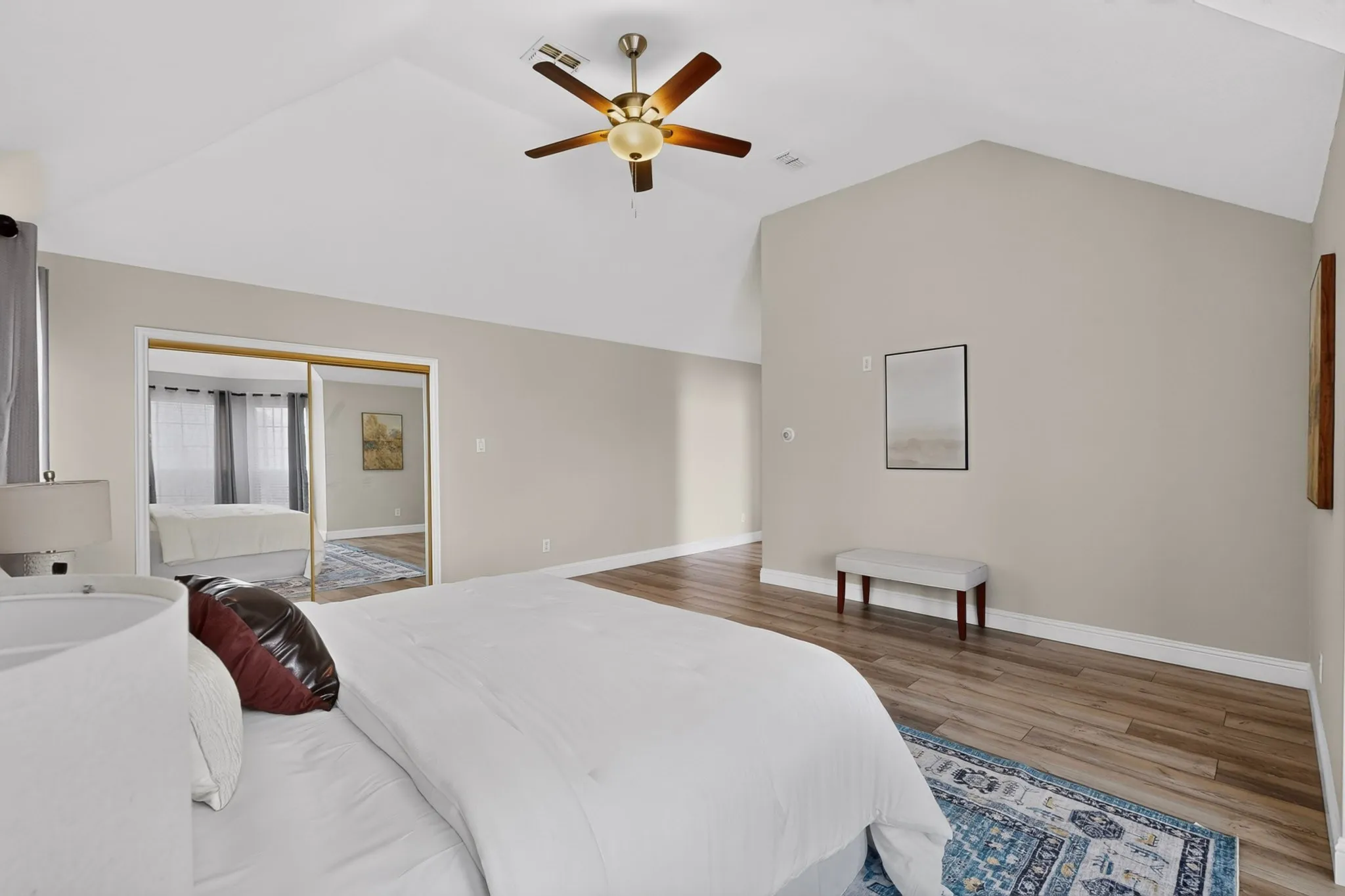 Vaulted ceiling bedroom featuring wood-finish flooring, a ceiling fan with light, and mirrored closet doors