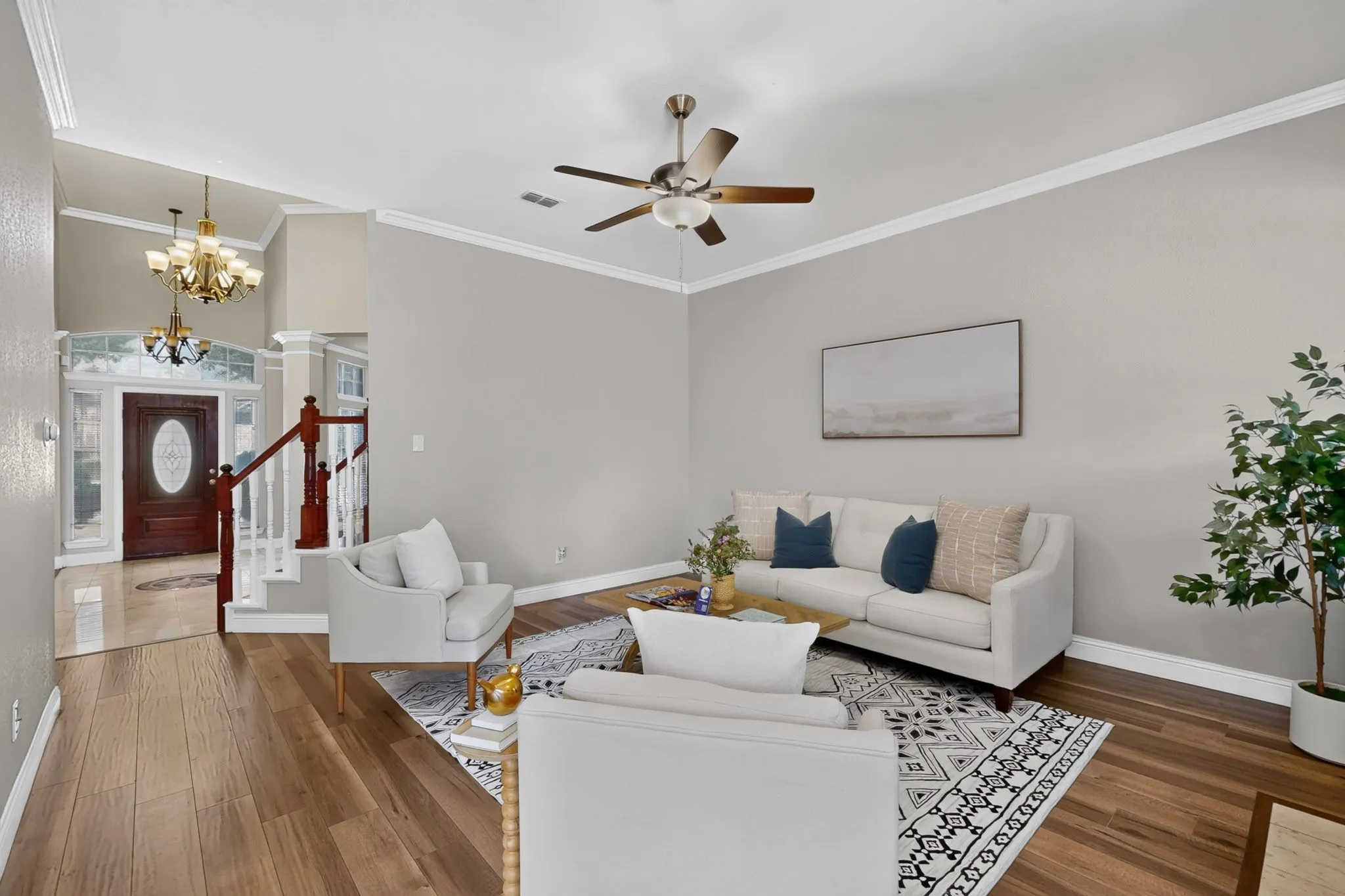Living area featuring wood-finish flooring, a ceiling fan with integrated lighting, and crown molding