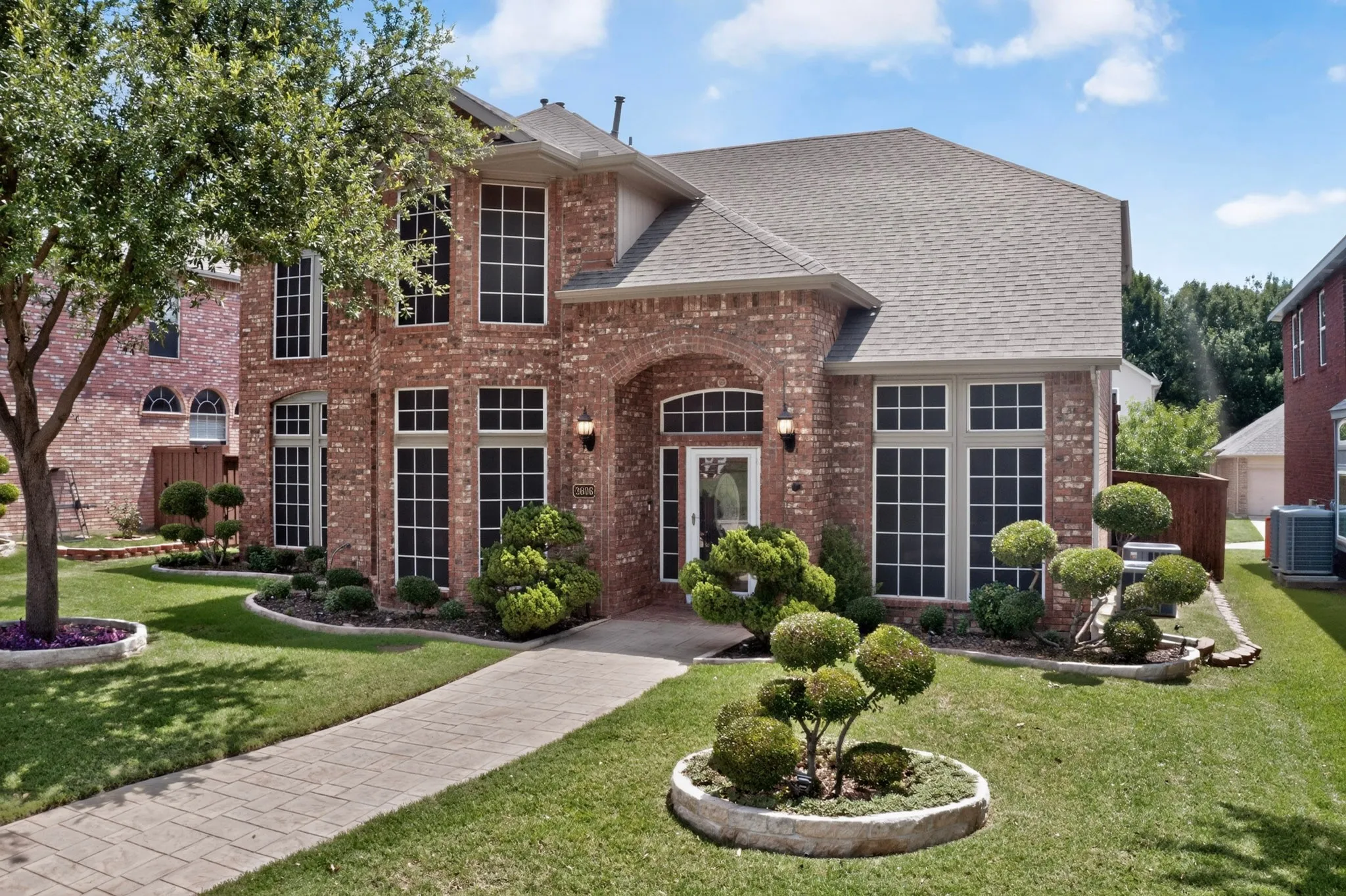 Brick facade residence featuring multiple large windows, a covered arched entryway, and a gabled roofline