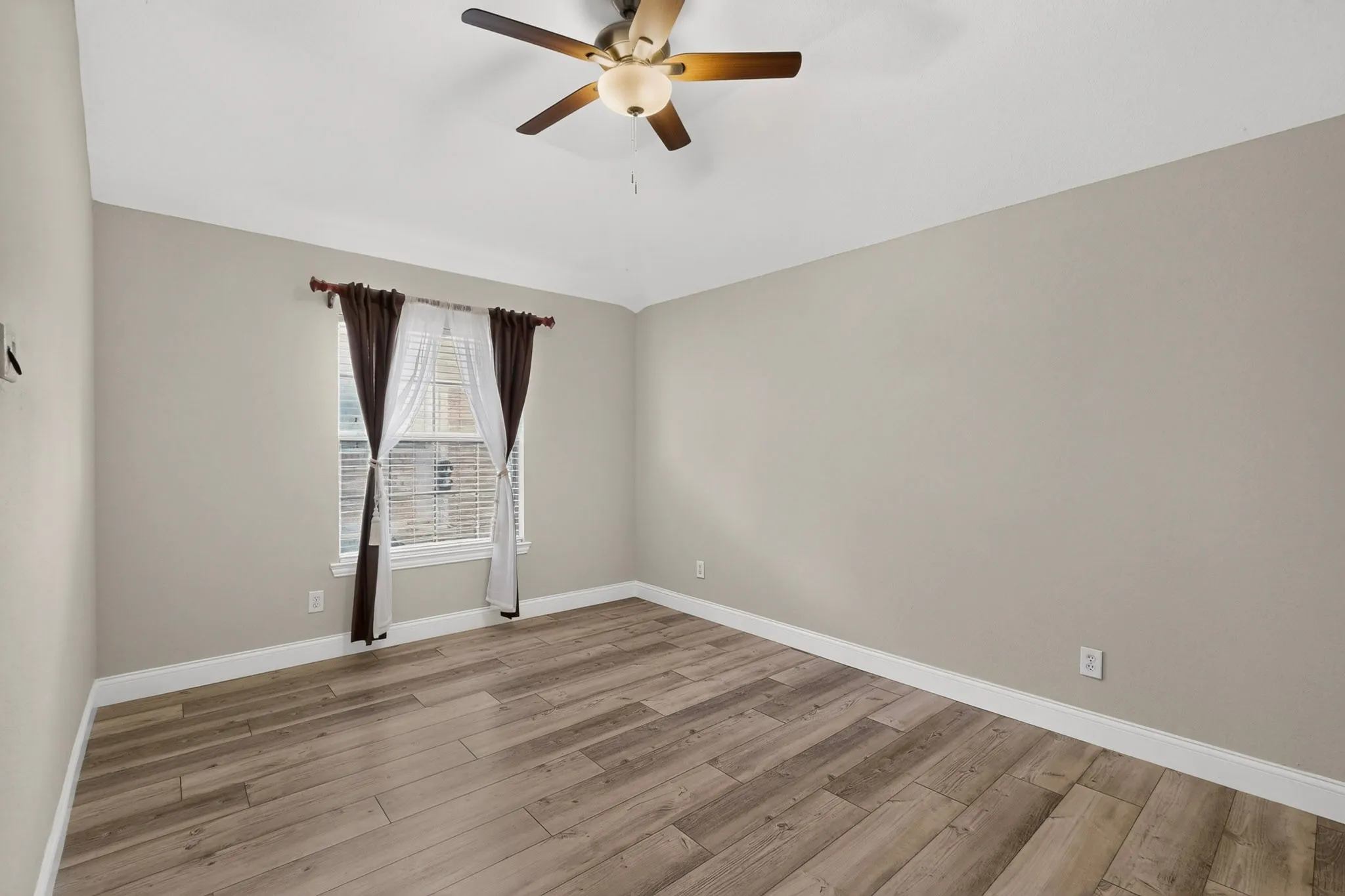 Light-filled room featuring wood-finish flooring, neutral wall tones, a ceiling fan, and white baseboards