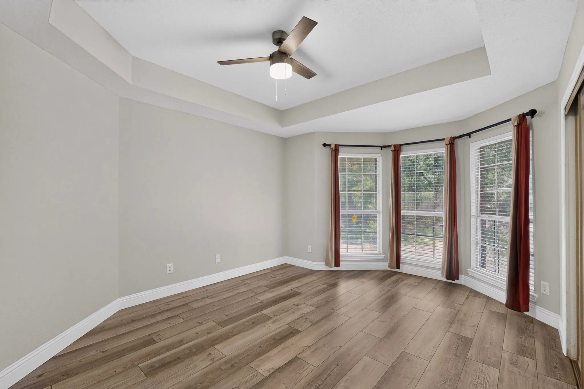 Spacious room featuring a tray ceiling, wood-finish flooring, and a modern ceiling fan