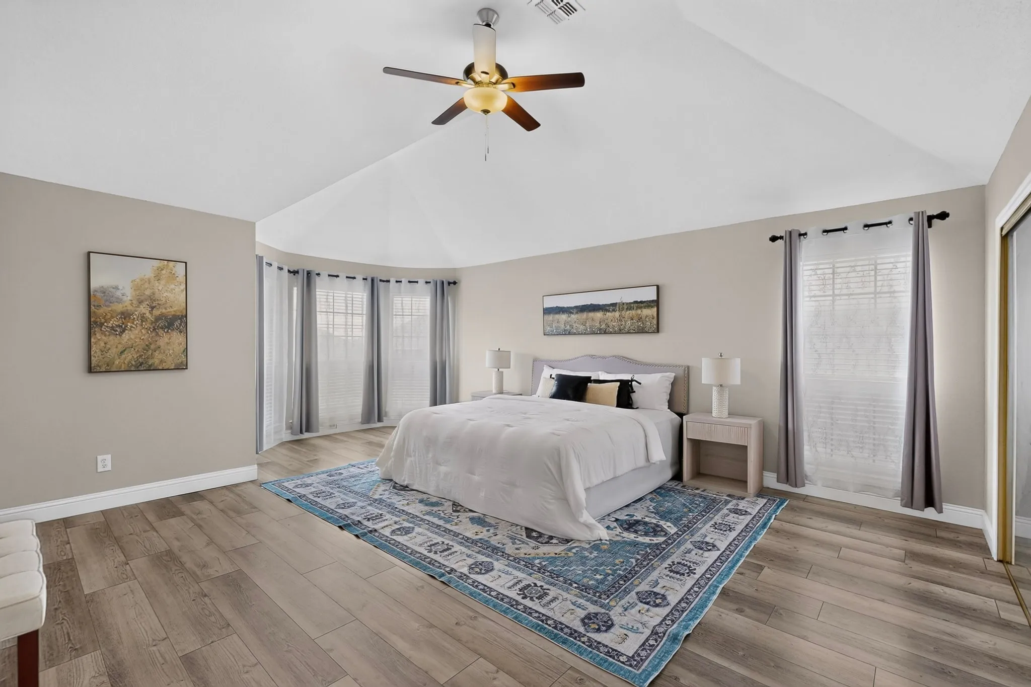 Vaulted ceilings featuring a ceiling fan, wood-finish flooring, and a curved window wall with multiple windows
